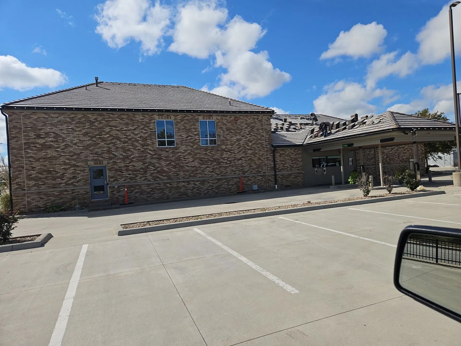 Brick building with a damaged roof and a parking lot on a sunny day.