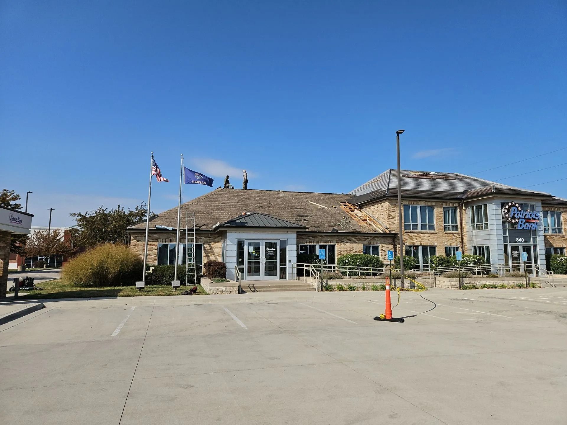 Building with damaged roof; flags and parking area in front.
