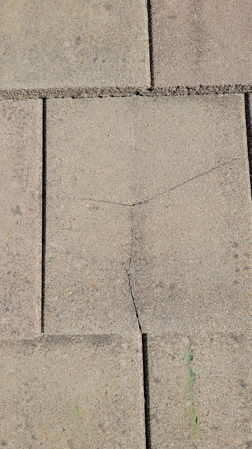 Overhead view of cracked paving stones in a light brown color.
