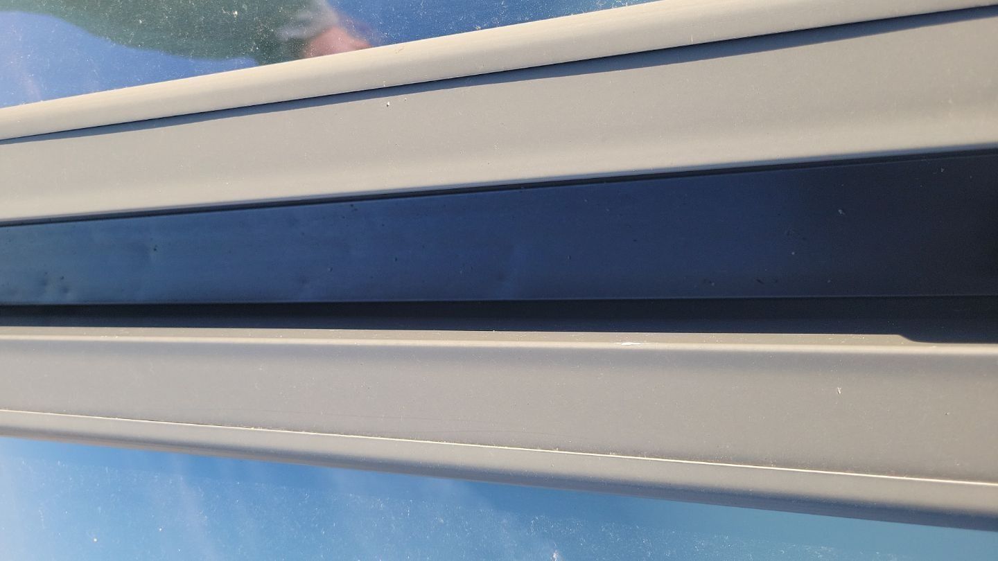 Close-up of a window frame with a seam; gray on blue.