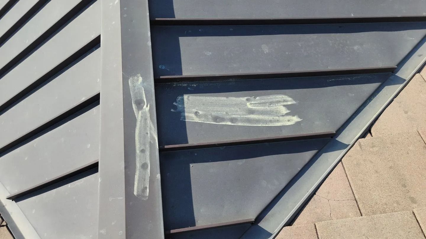 Gray metal roof flashing with patched areas, attached to a roof with brown shingles.