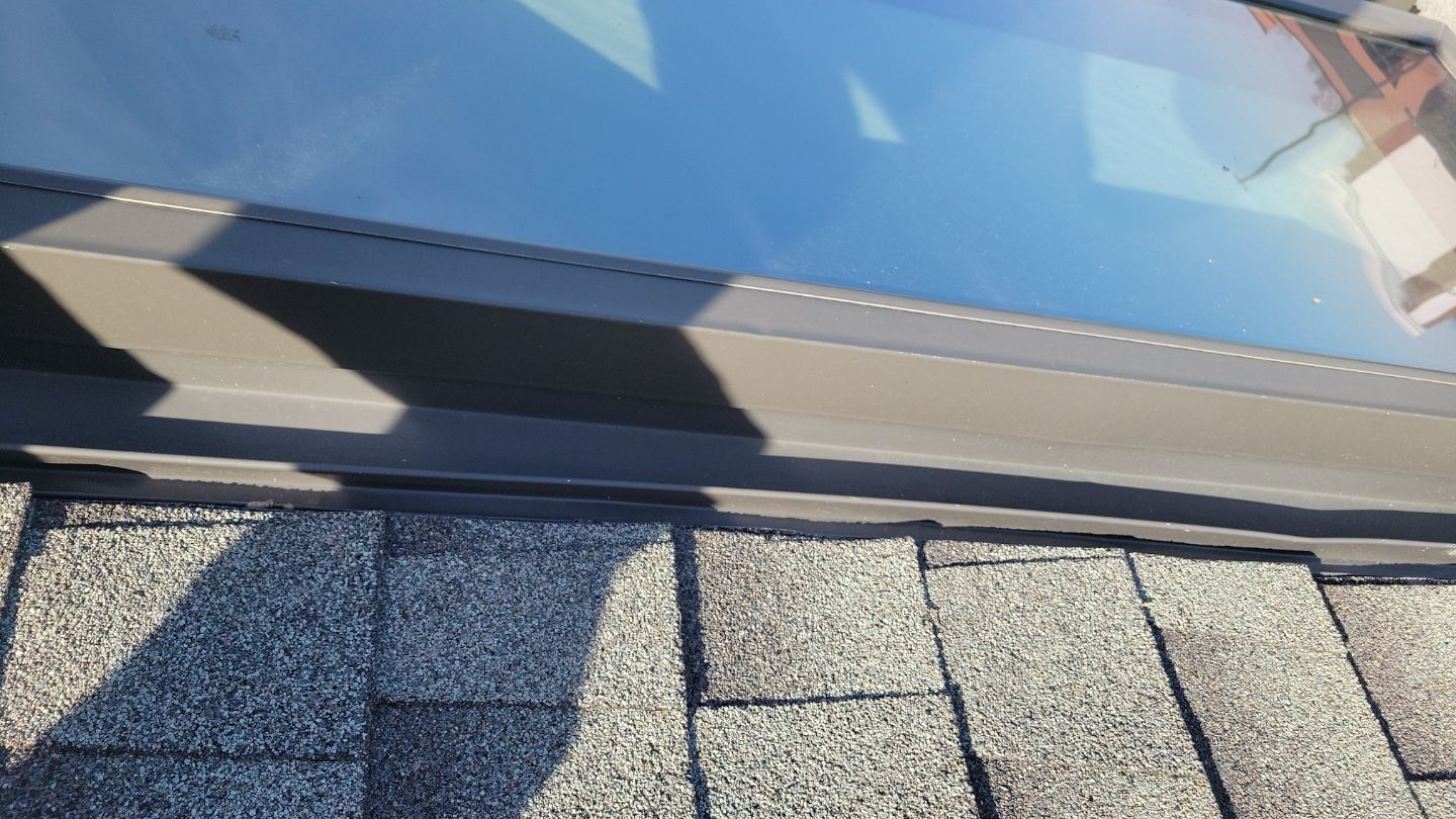 Skylight on a shingled roof, showing the edge where glass meets the dark frame.