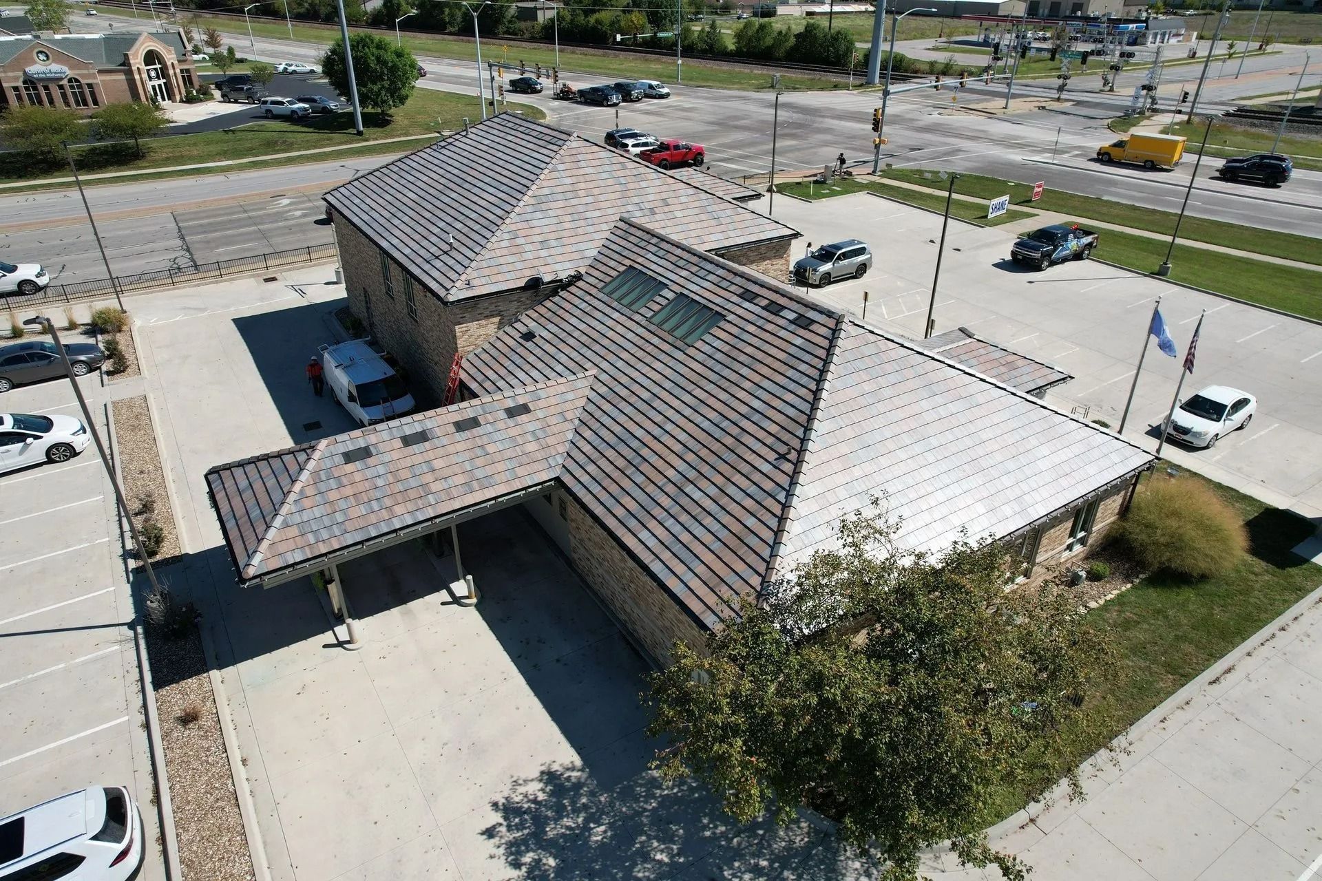 Aerial view of a brown brick building with a sloped roof and a parking lot filled with cars.