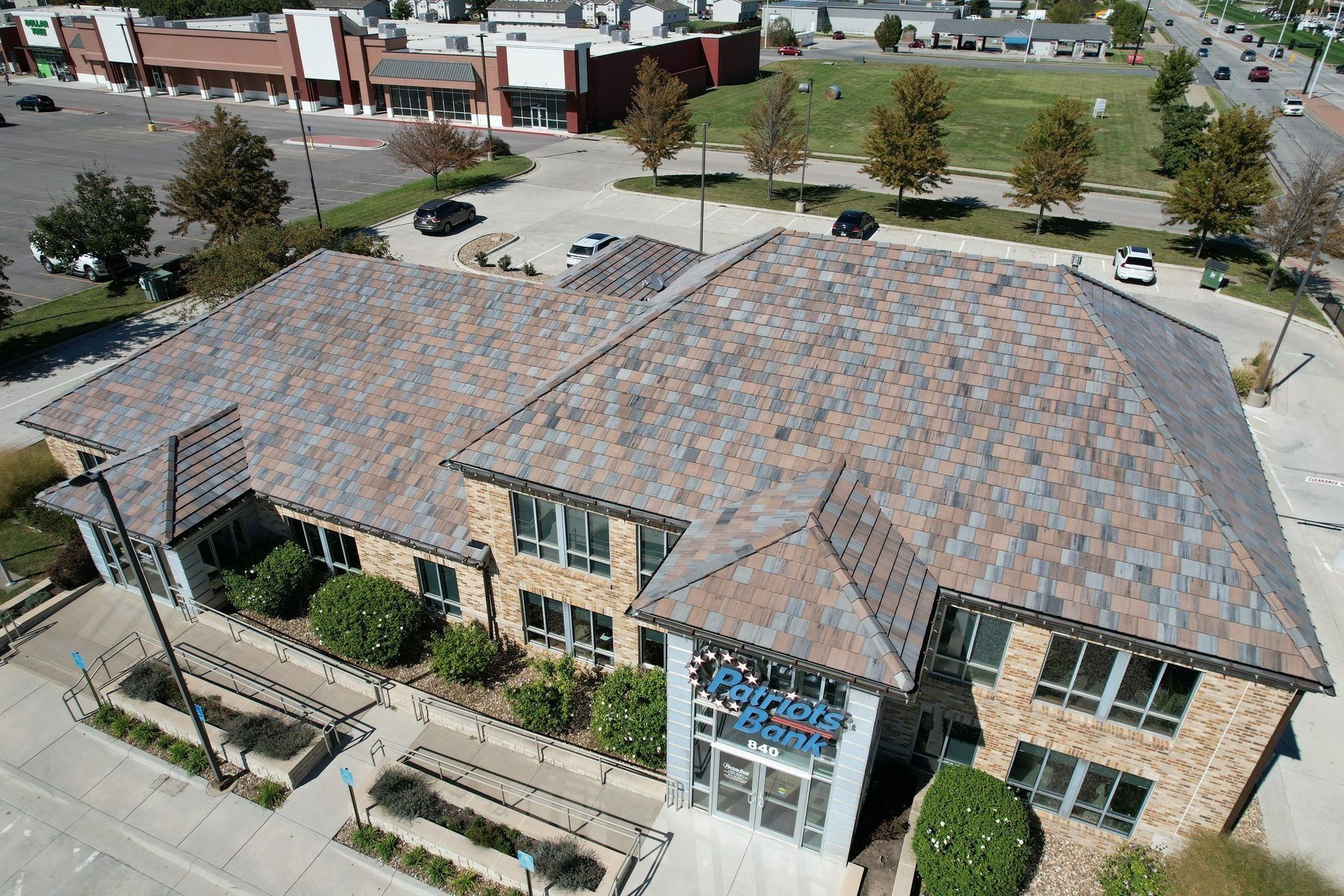 Aerial view of a two-story building with a multi-colored slate roof, next to a parking lot and grassy area.
