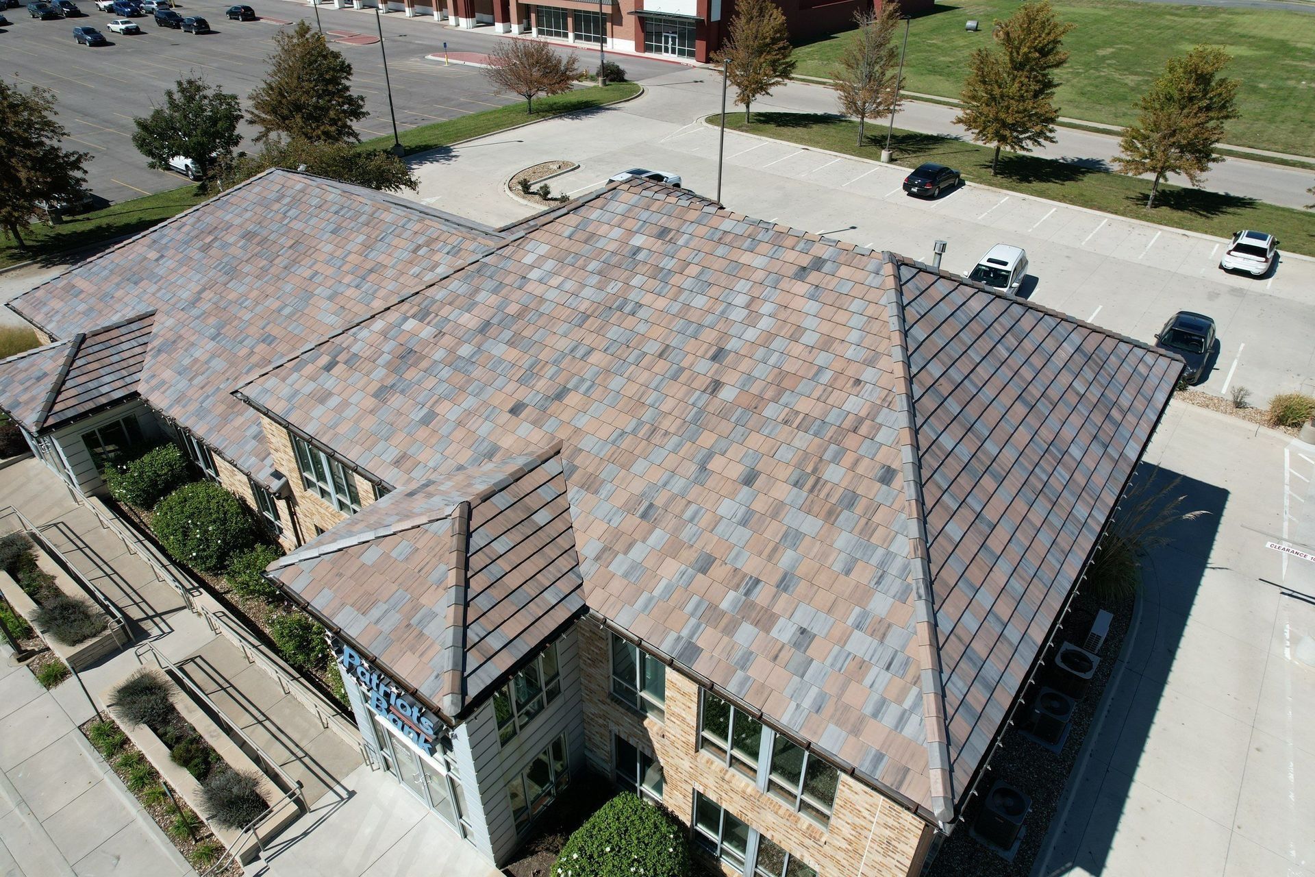 Overhead view of a building with a multi-colored tile roof, near a parking lot and green space.