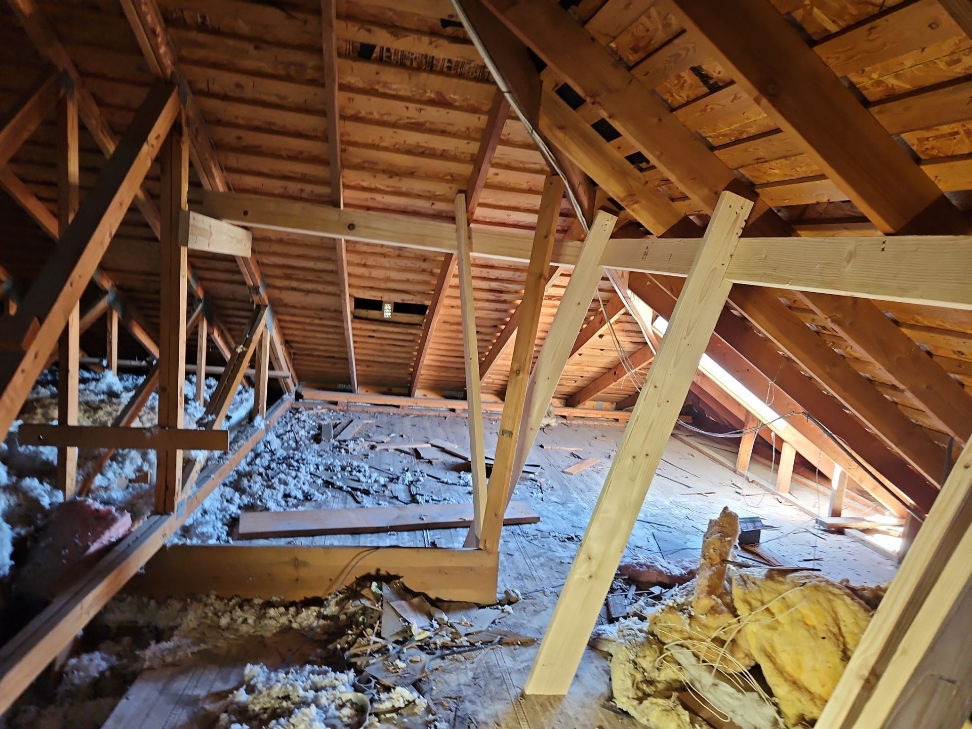 Attic interior with exposed wooden rafters, insulation, and debris on the floor.