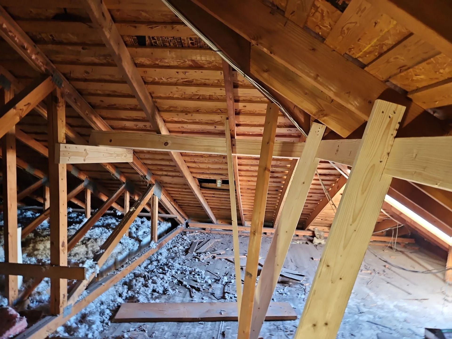 Wooden attic framing, beams and rafters, with insulation on the floor.