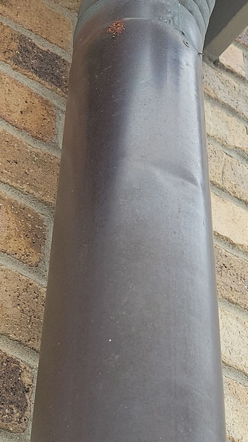 Brown downspout against a brick wall.