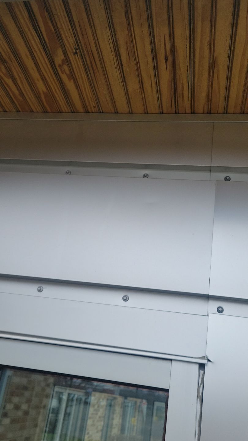 Exterior view of building with light gray metal siding and brown wood ceiling.