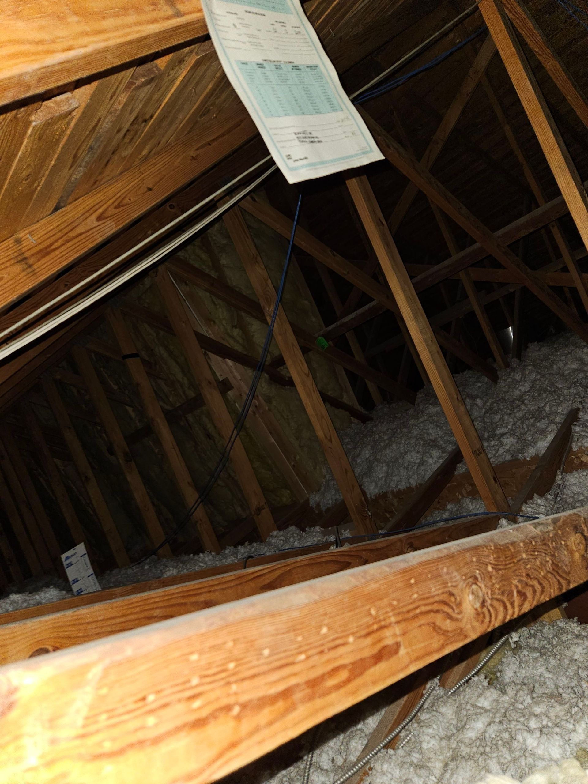 Interior of an attic with wooden beams, insulation, and a hanging document.