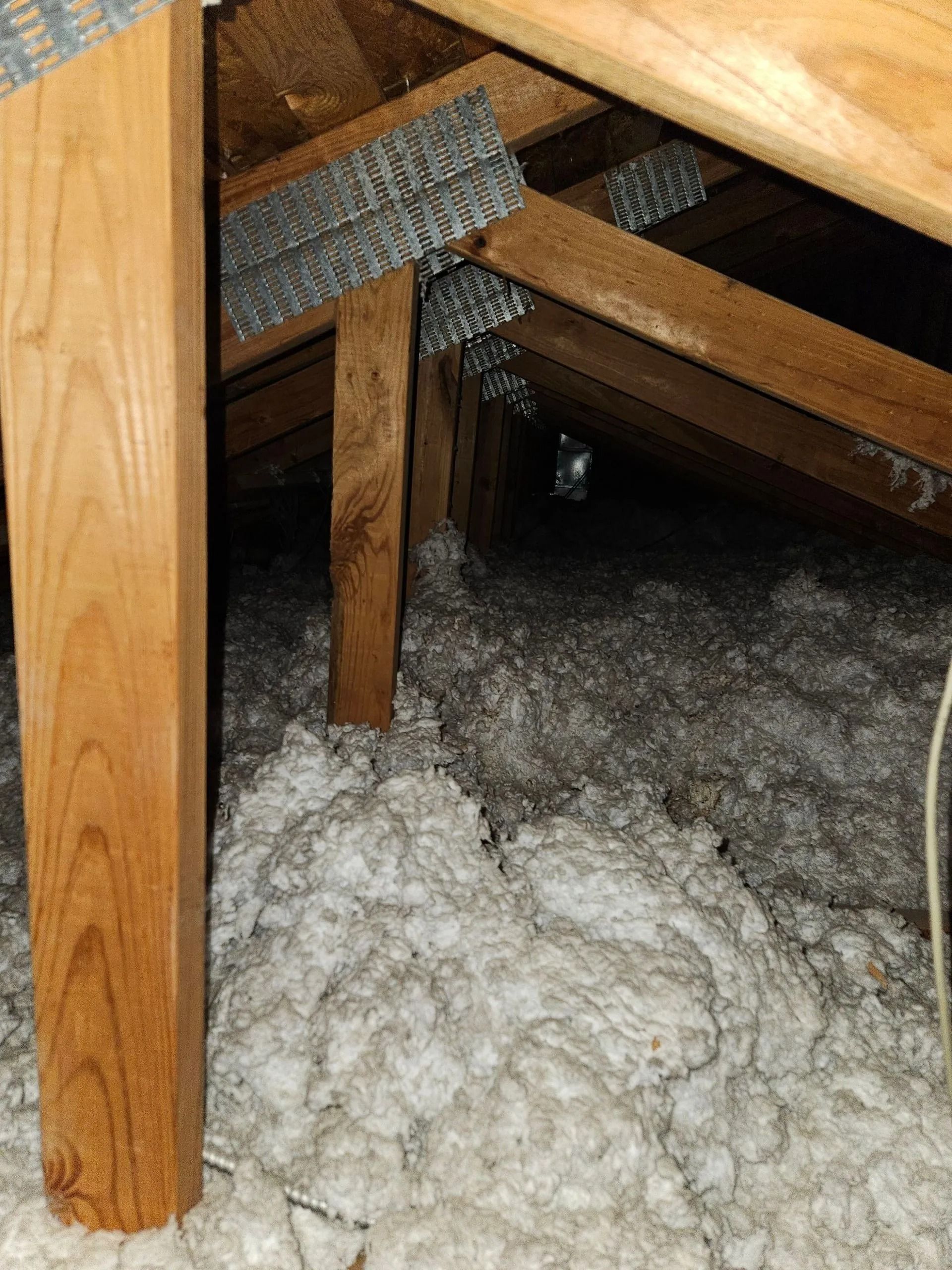 Attic view with wooden beams, metal connectors, and white insulation.