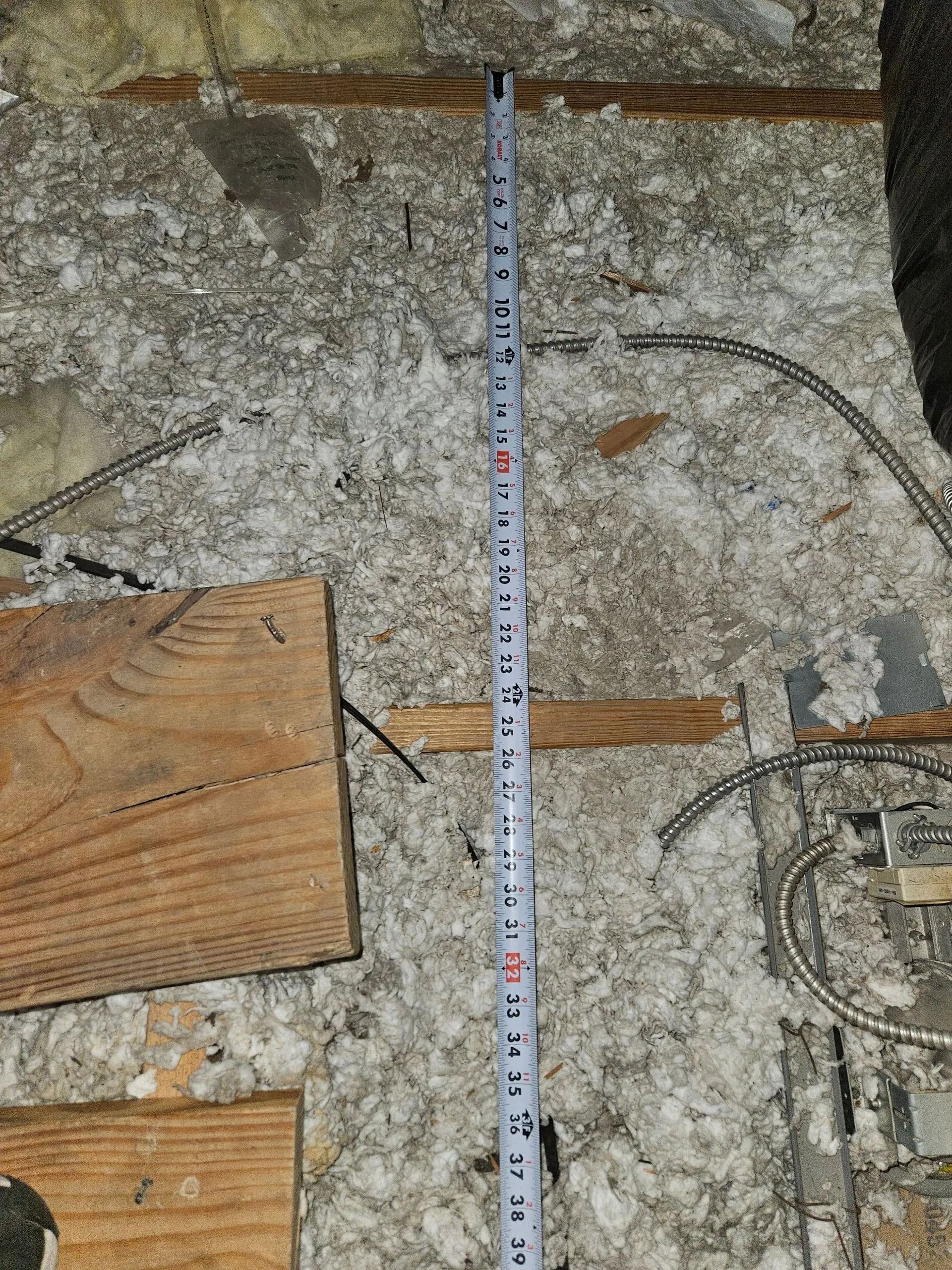 Measuring tape on insulation in a floor with exposed wood and metal wire.