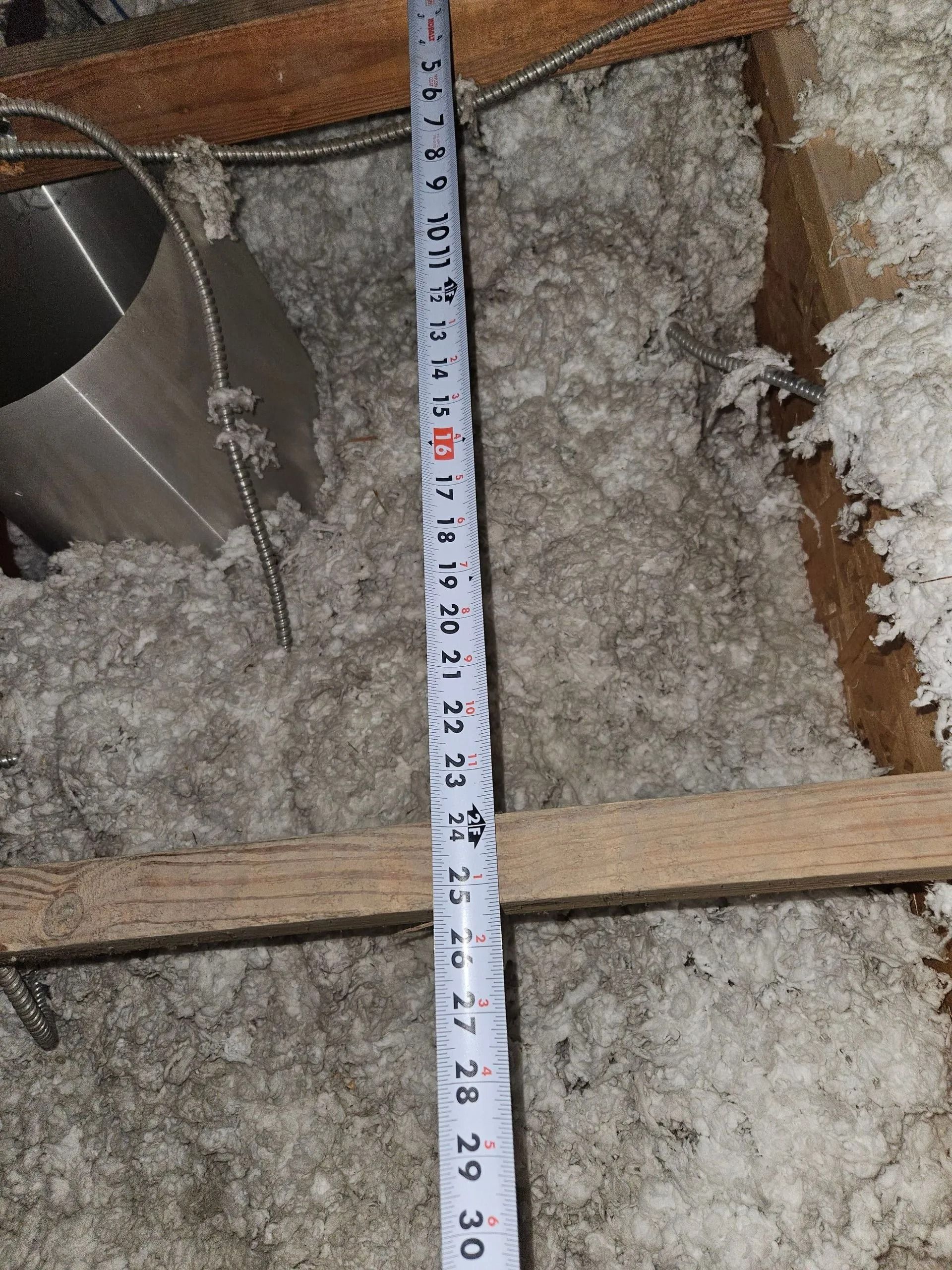 Tape measure held up against insulation in an attic. The measurement reads to about 30 inches.