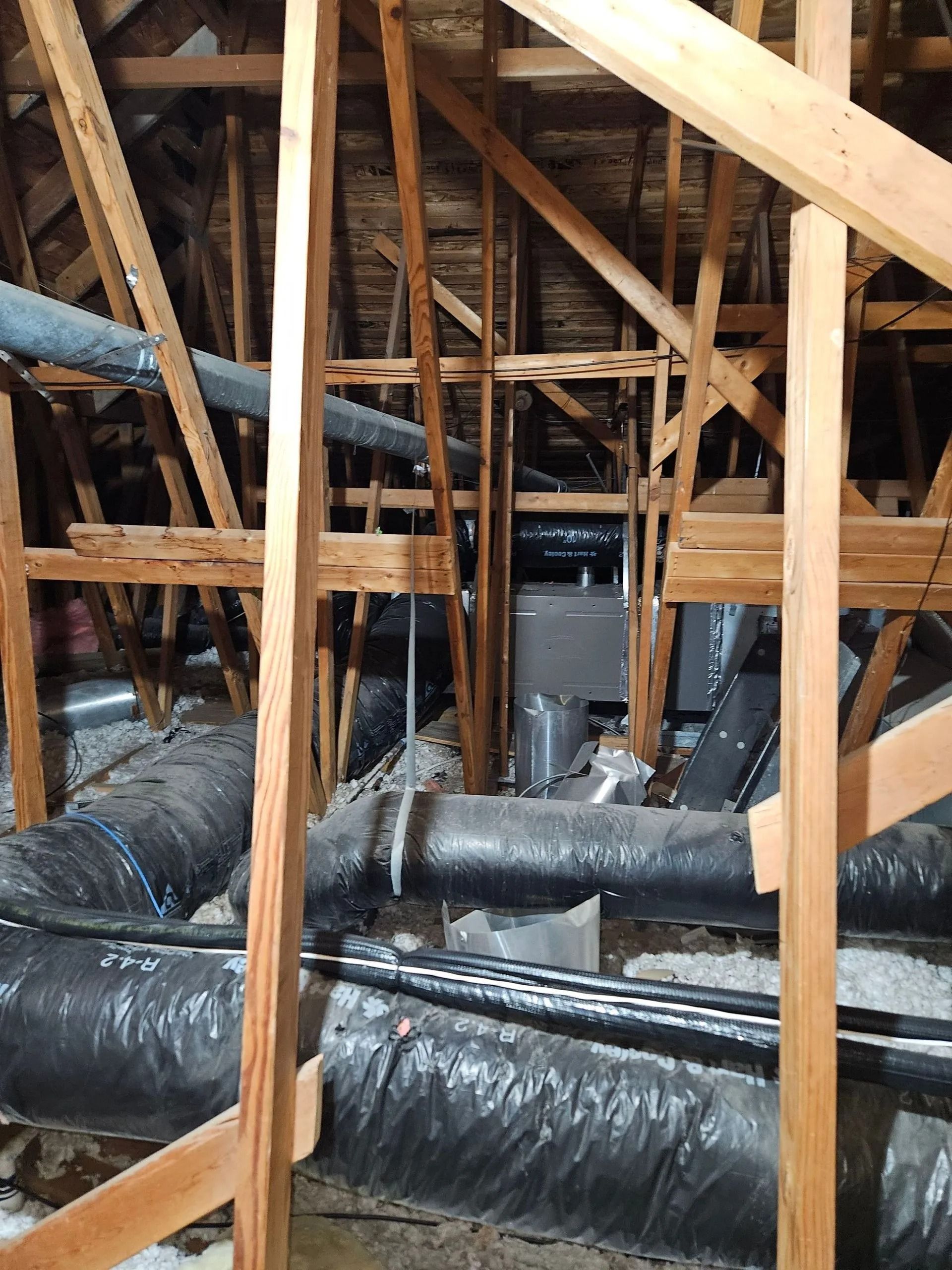 Interior view of an attic with wooden rafters, ductwork, and a central heating/cooling unit.