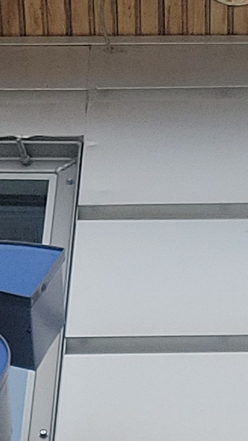 Exterior corner of building with window. Metal trim and blue sign. White siding and wooden upper edge.