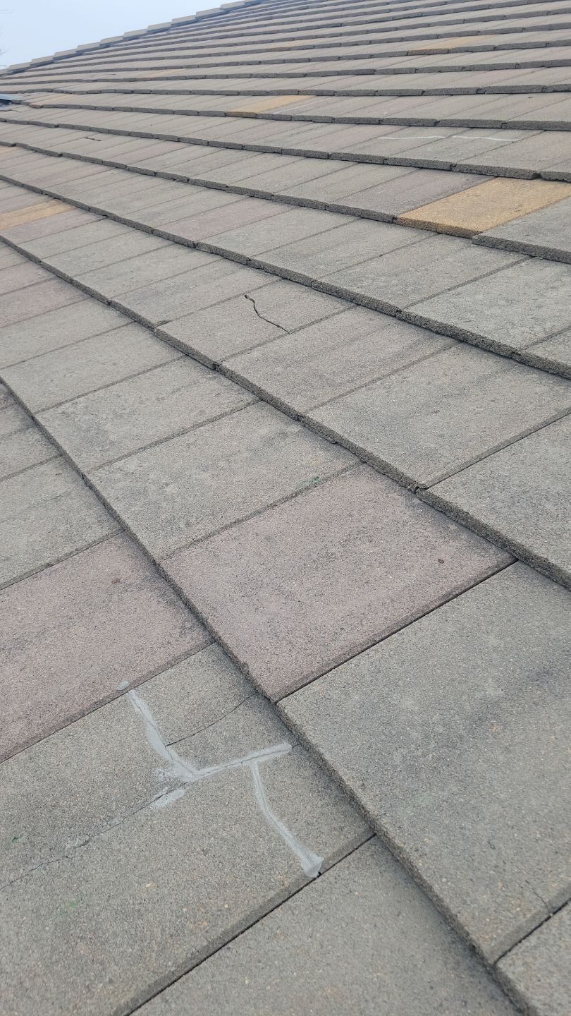 Close-up of a tiled roof. Gray concrete tiles with visible cracks and some light discoloration.