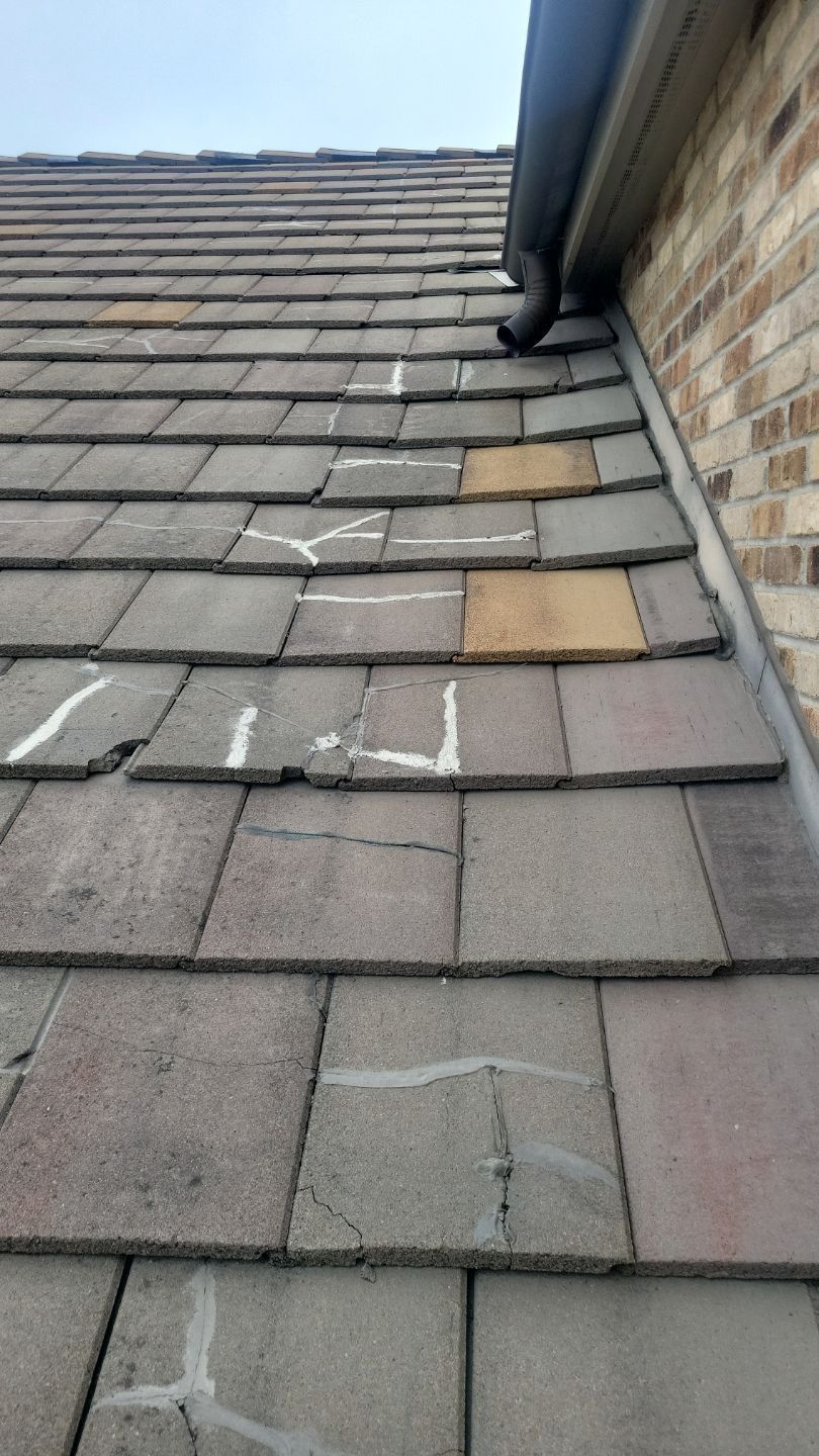 Close-up of a damaged asphalt shingle roof. Several shingles are cracked and have white sealant.