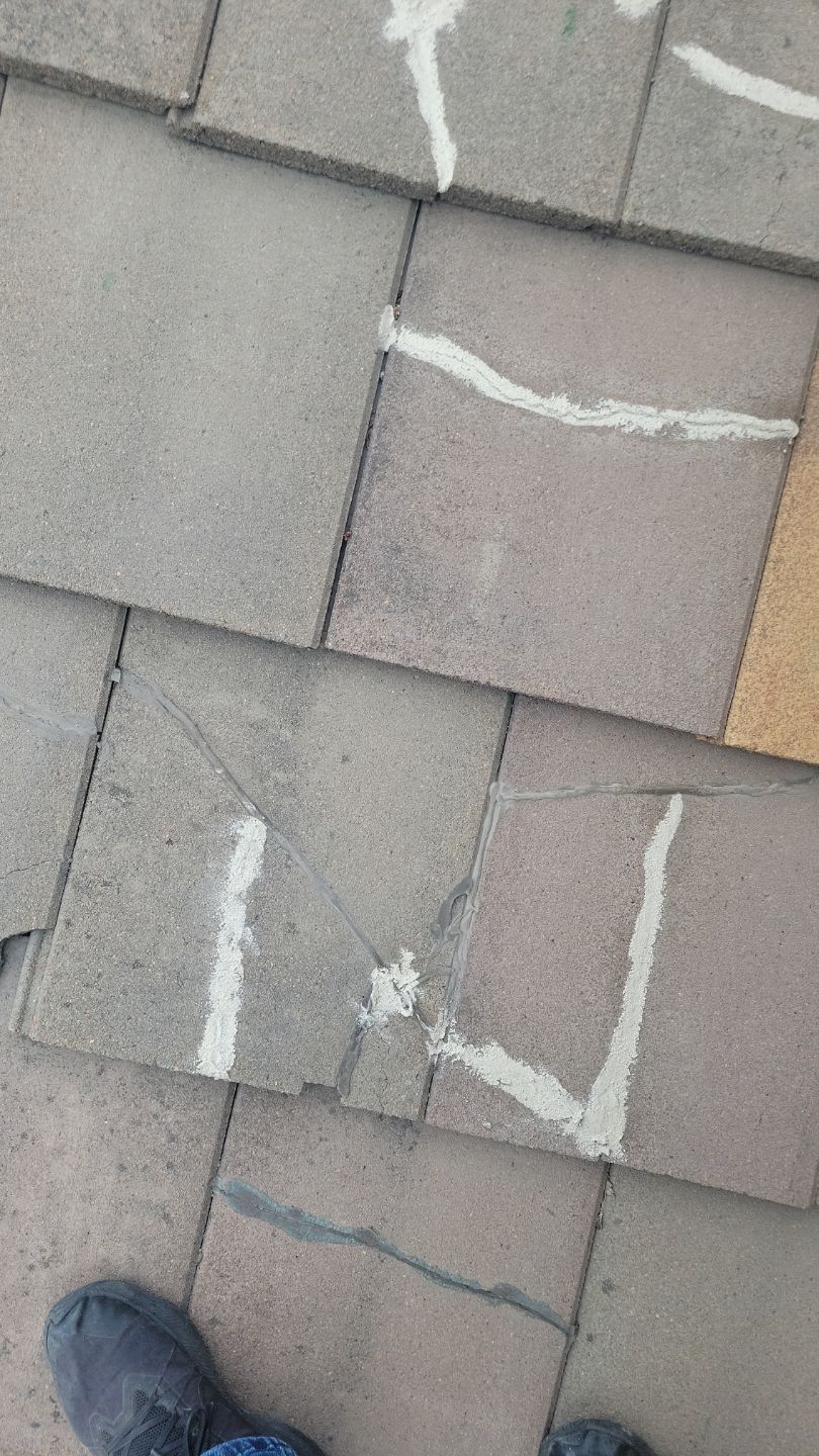 Close-up of gray asphalt shingles with white sealant applied along cracks.