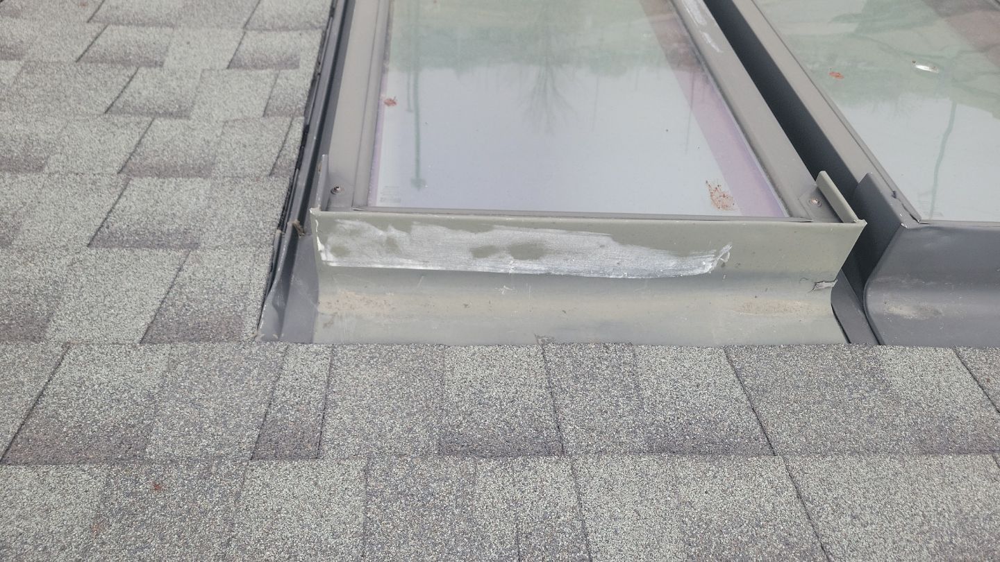 Close-up of a roof with shingles and a skylight. Silver flashing shows some wear.