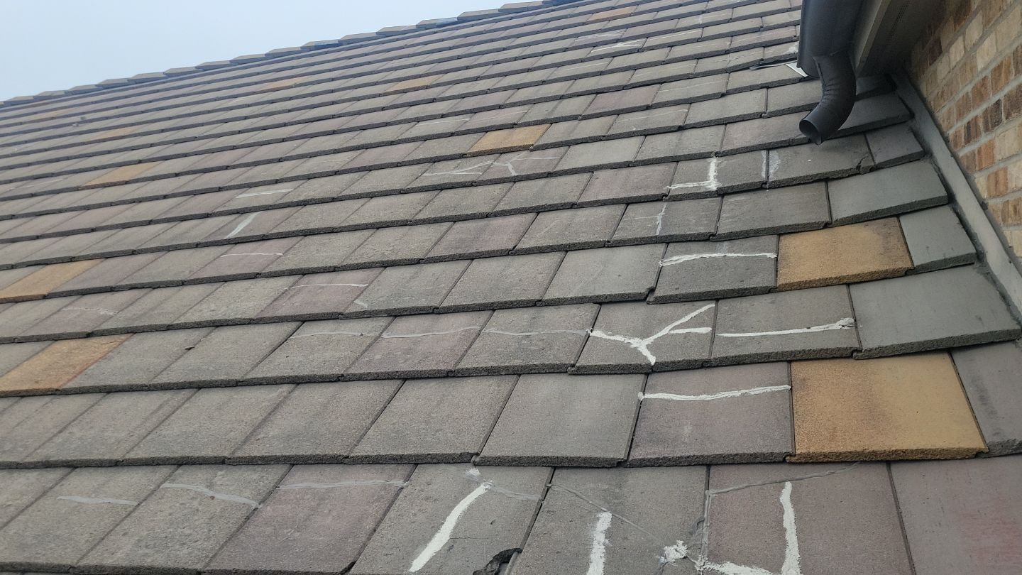 Close-up of a tiled roof; several tiles are cracked and marked with white chalk for repair.