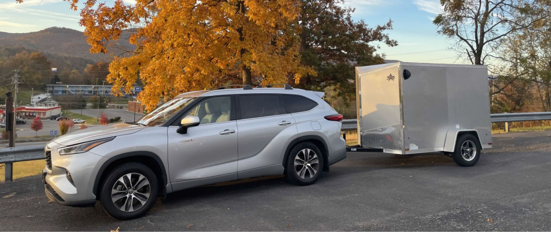 A silver SUV is towing a trailer in a parking lot