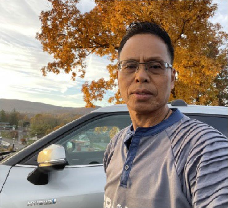 A man wearing glasses is standing in front of a car