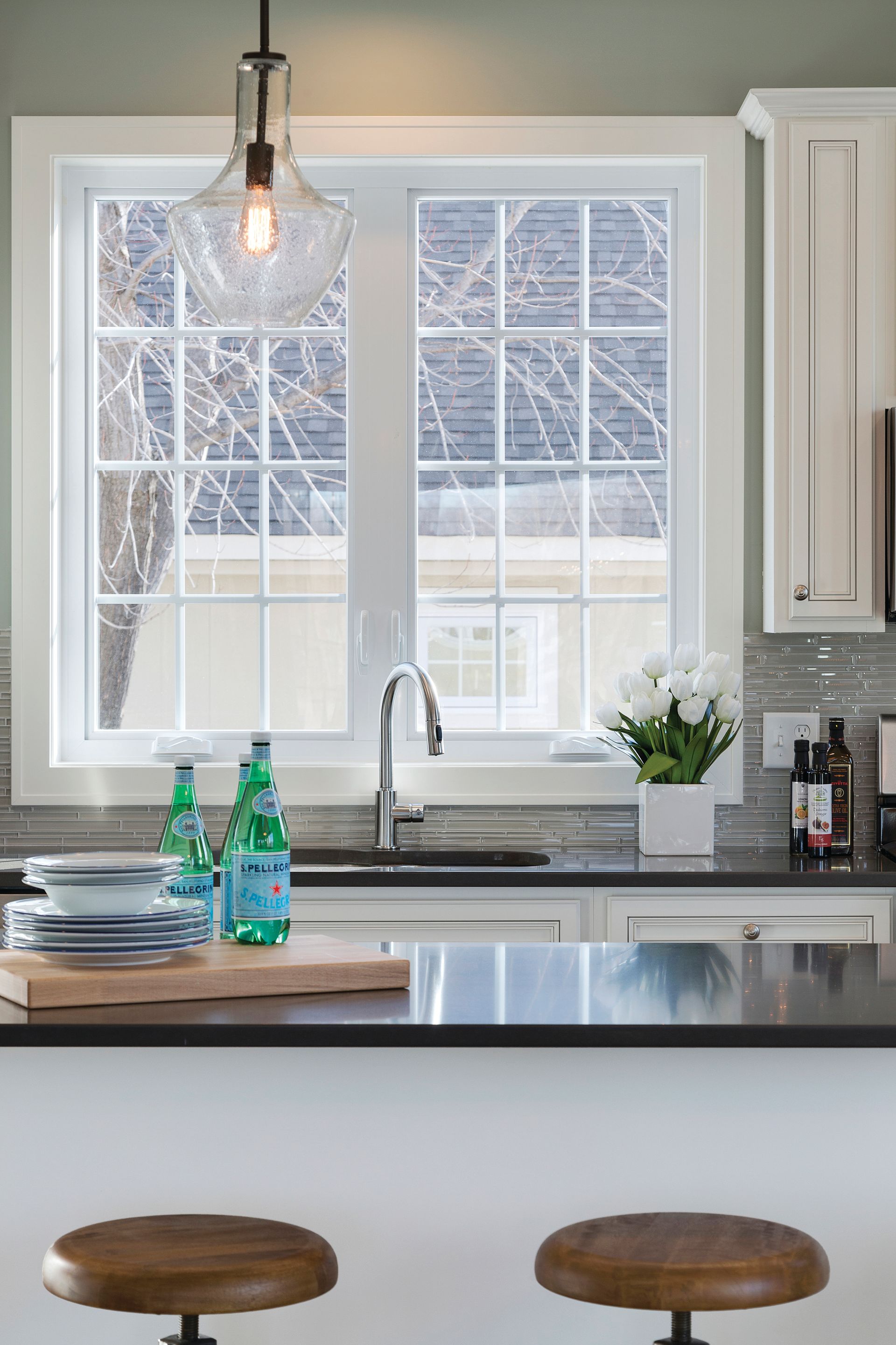 A kitchen with two bar stools , a sink , and a window.