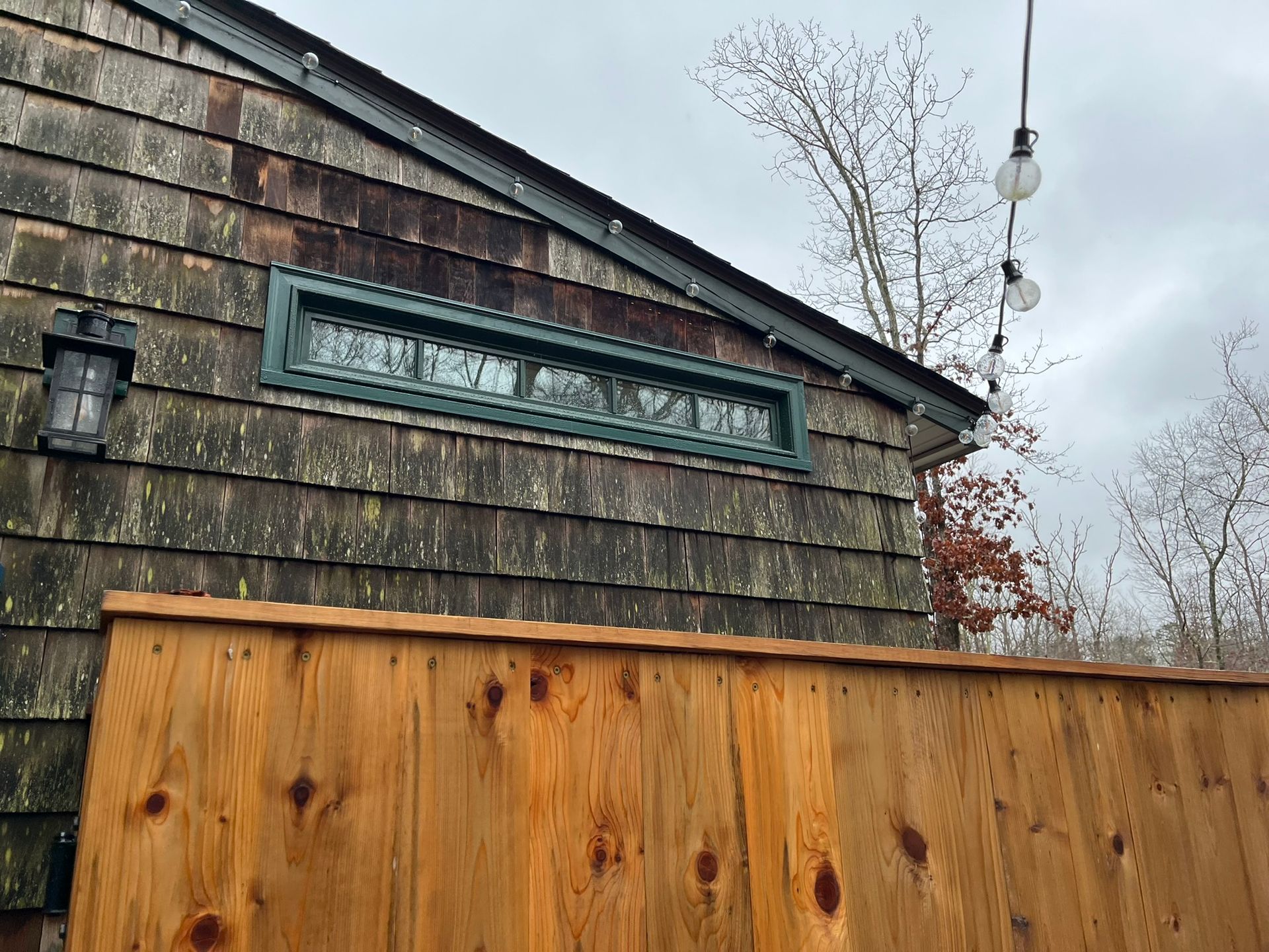 A wooden fence is in front of a house with shingles on the roof.