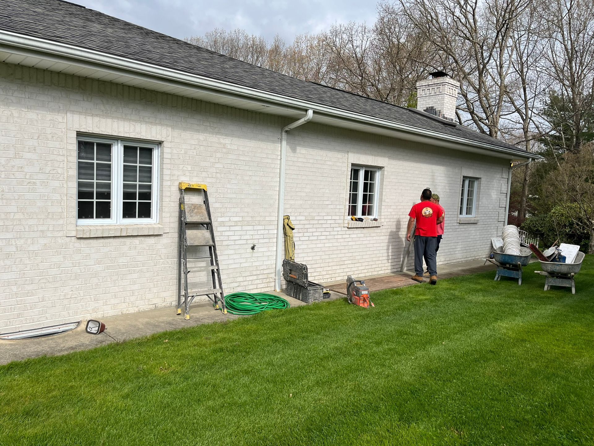 A man in a red shirt is standing in front of a white brick house.
