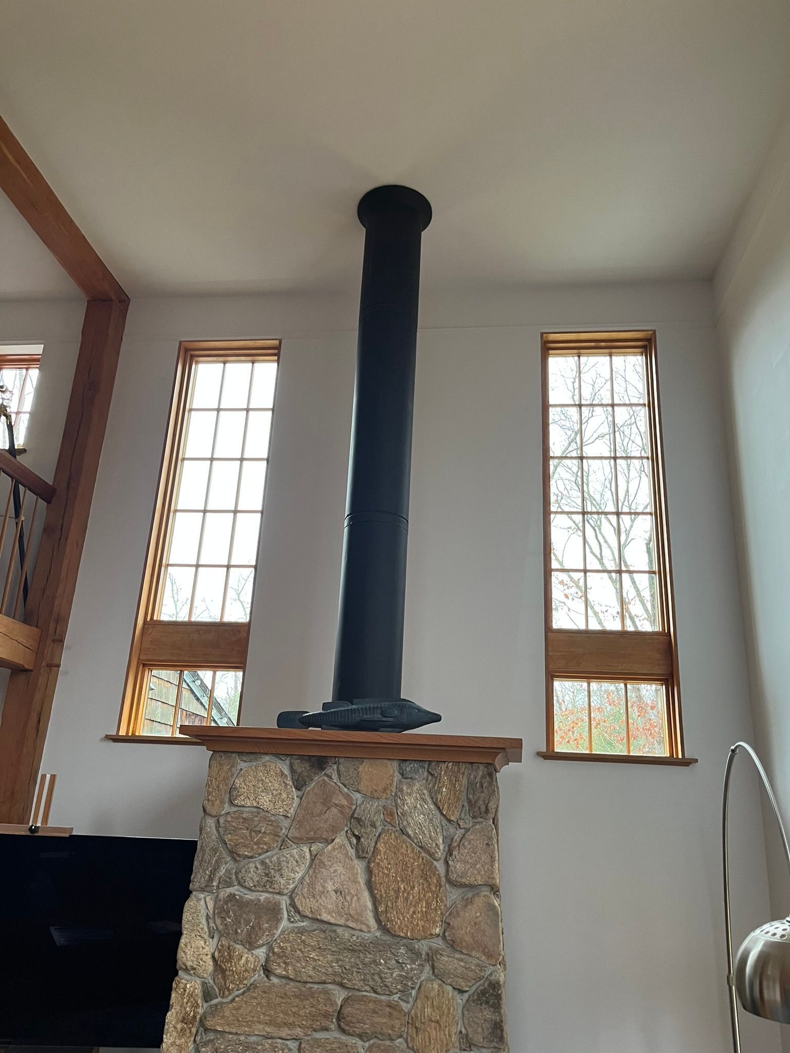 A stone fireplace with a chimney hanging from the ceiling in a room with windows.