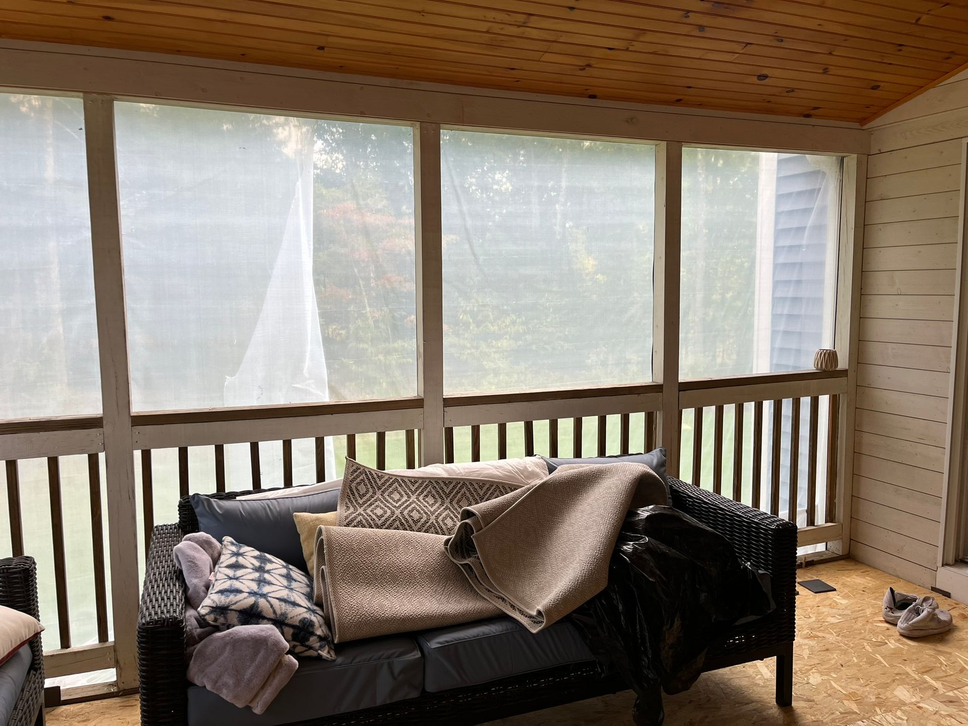 A screened in porch with a couch, chairs, and a railing.
