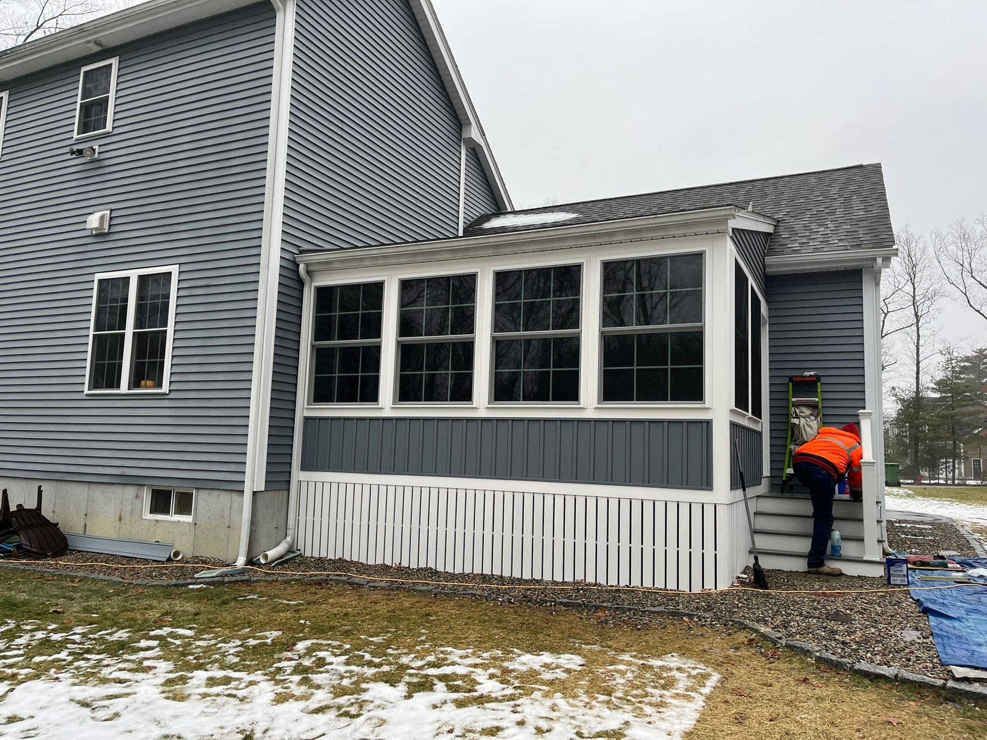 A man is standing on the steps of a screened in porch next to a house.