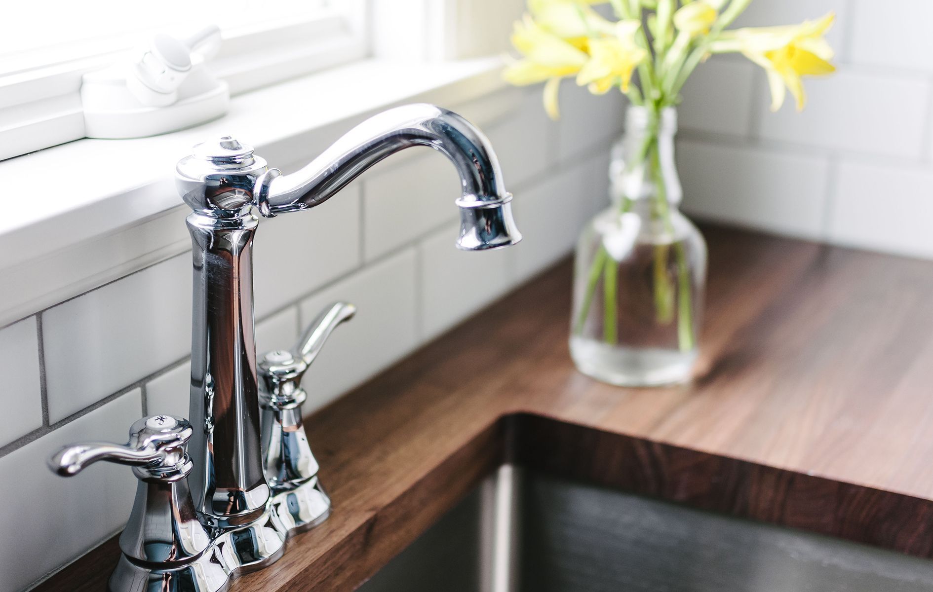 A kitchen sink with a faucet and a vase of flowers on the counter.