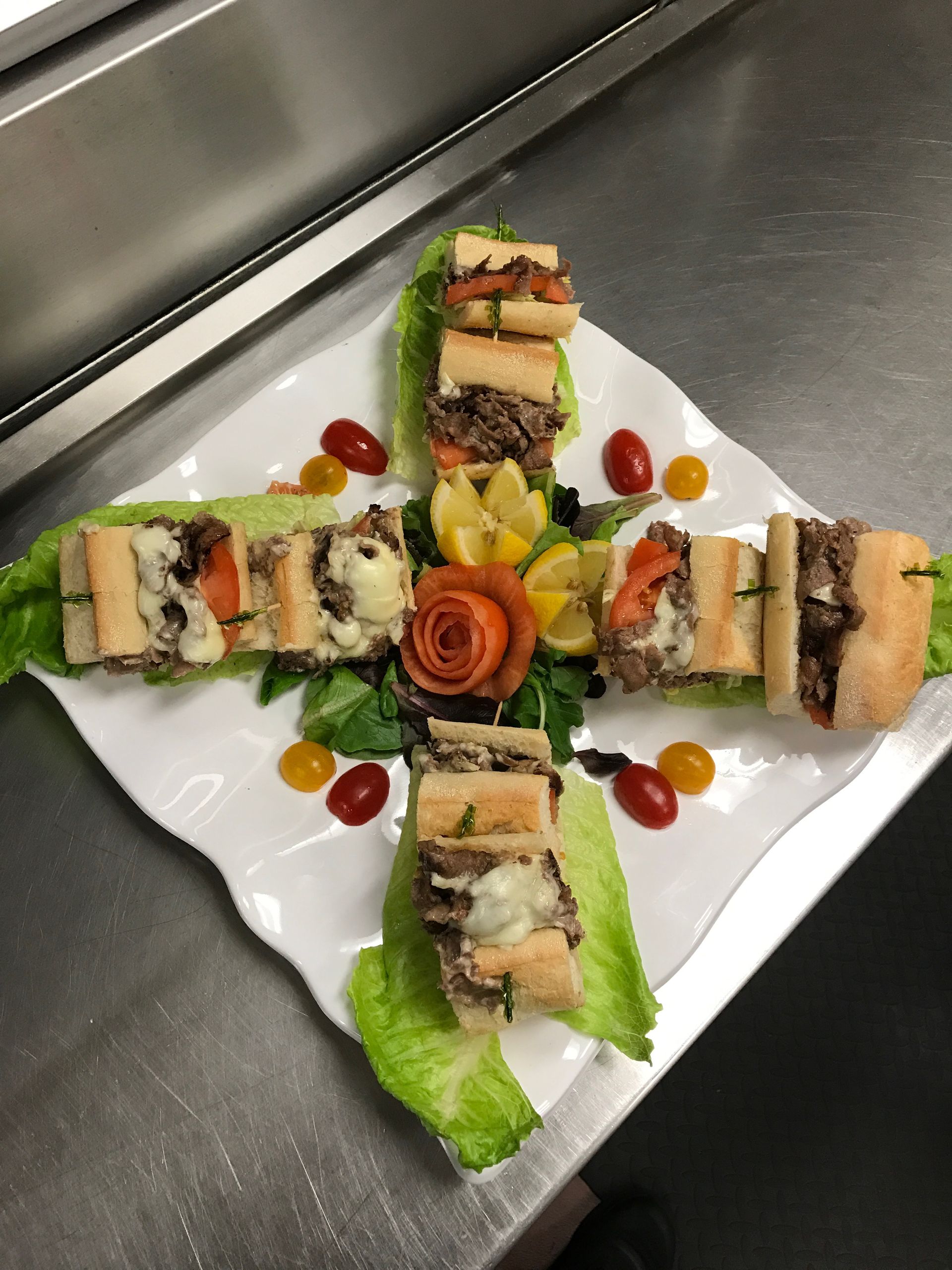 Plated appetizer of rolled sandwiches arranged in a cross on a white square plate with garnish and sauce dots