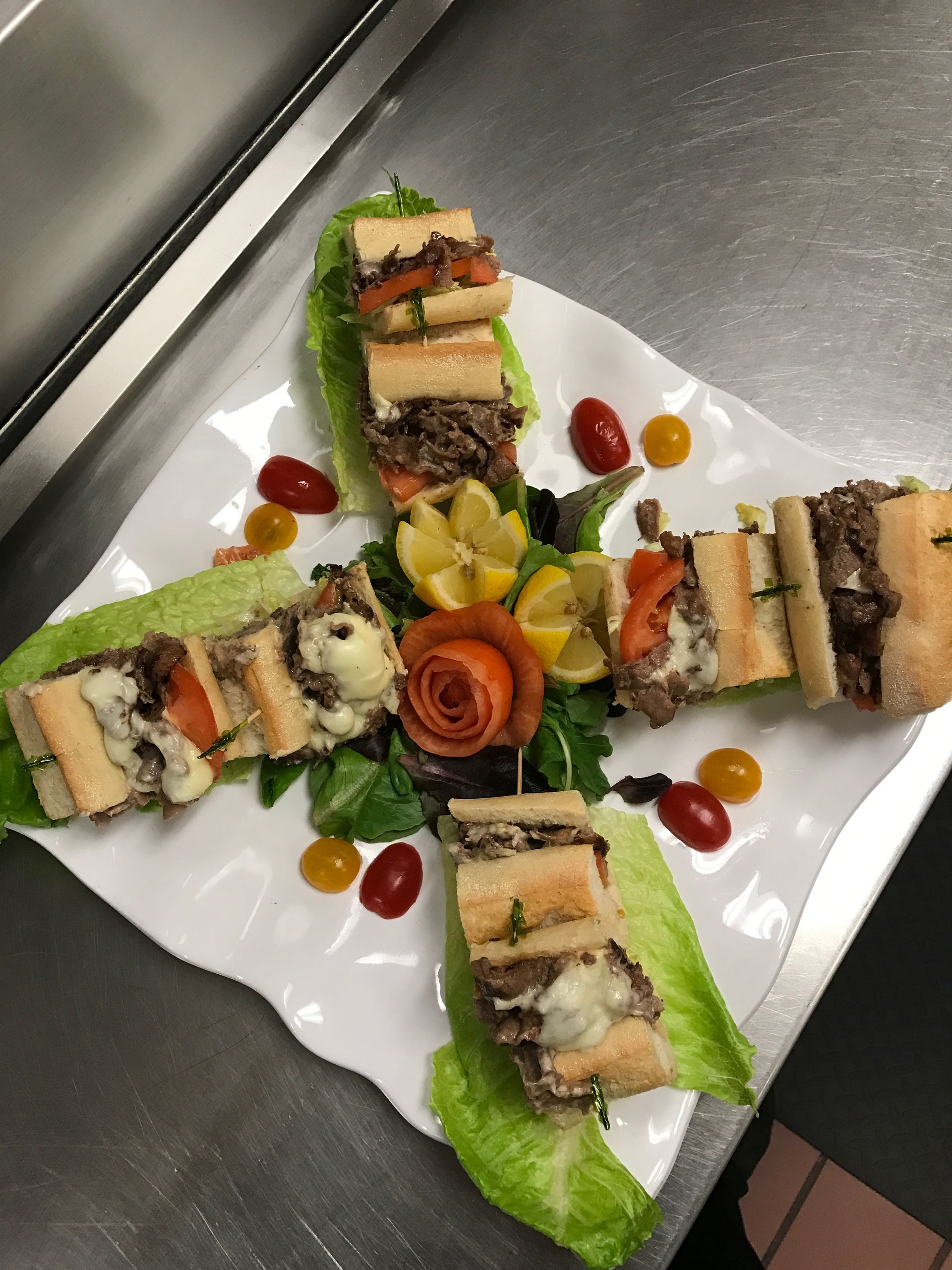 Four savory sandwiches arranged around a garnish of vegetables and cherry tomatoes on a white plate