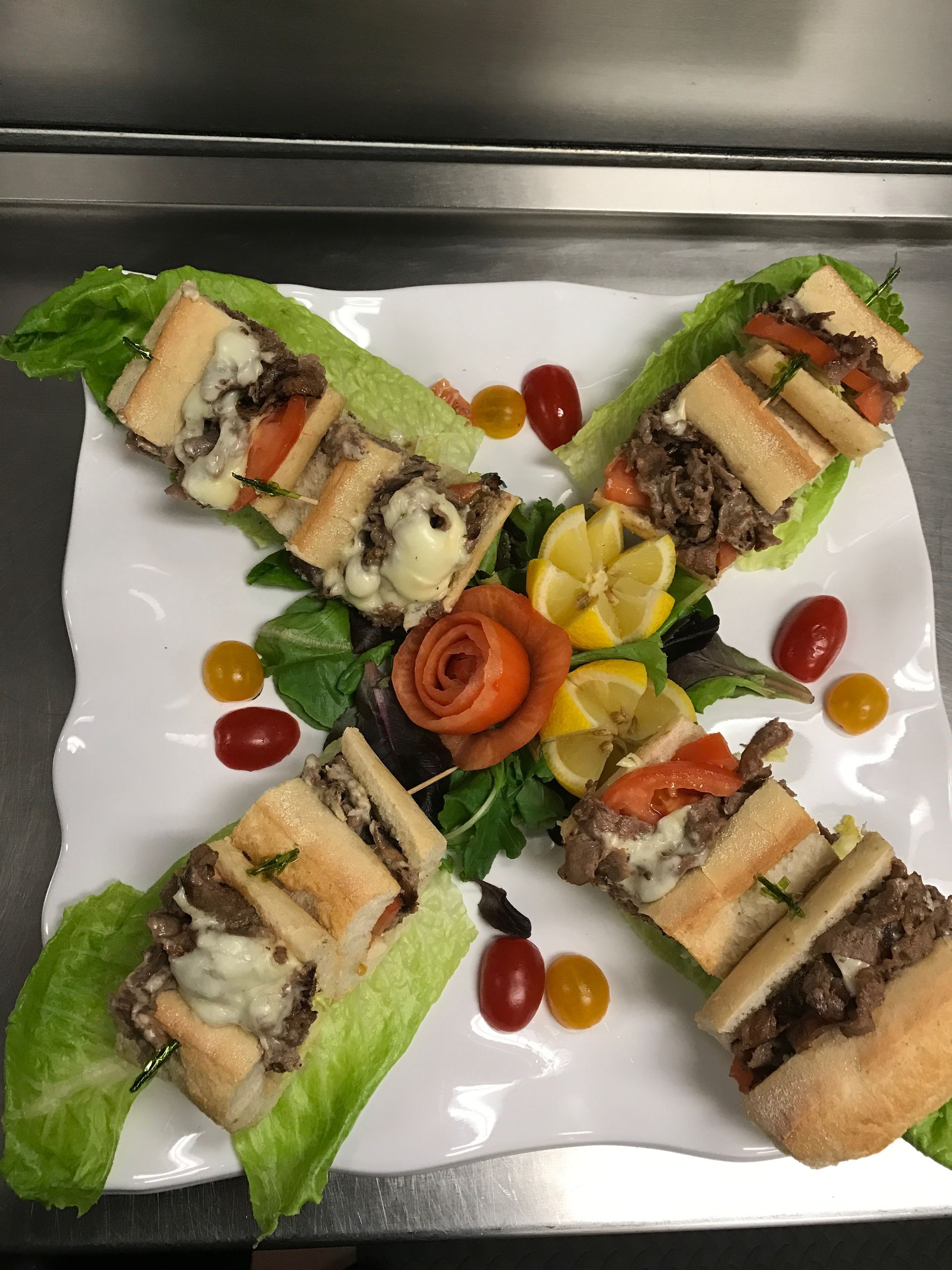 Four toasted sandwiches arranged in a square on a white plate, garnished with greens and cherry tomatoes.