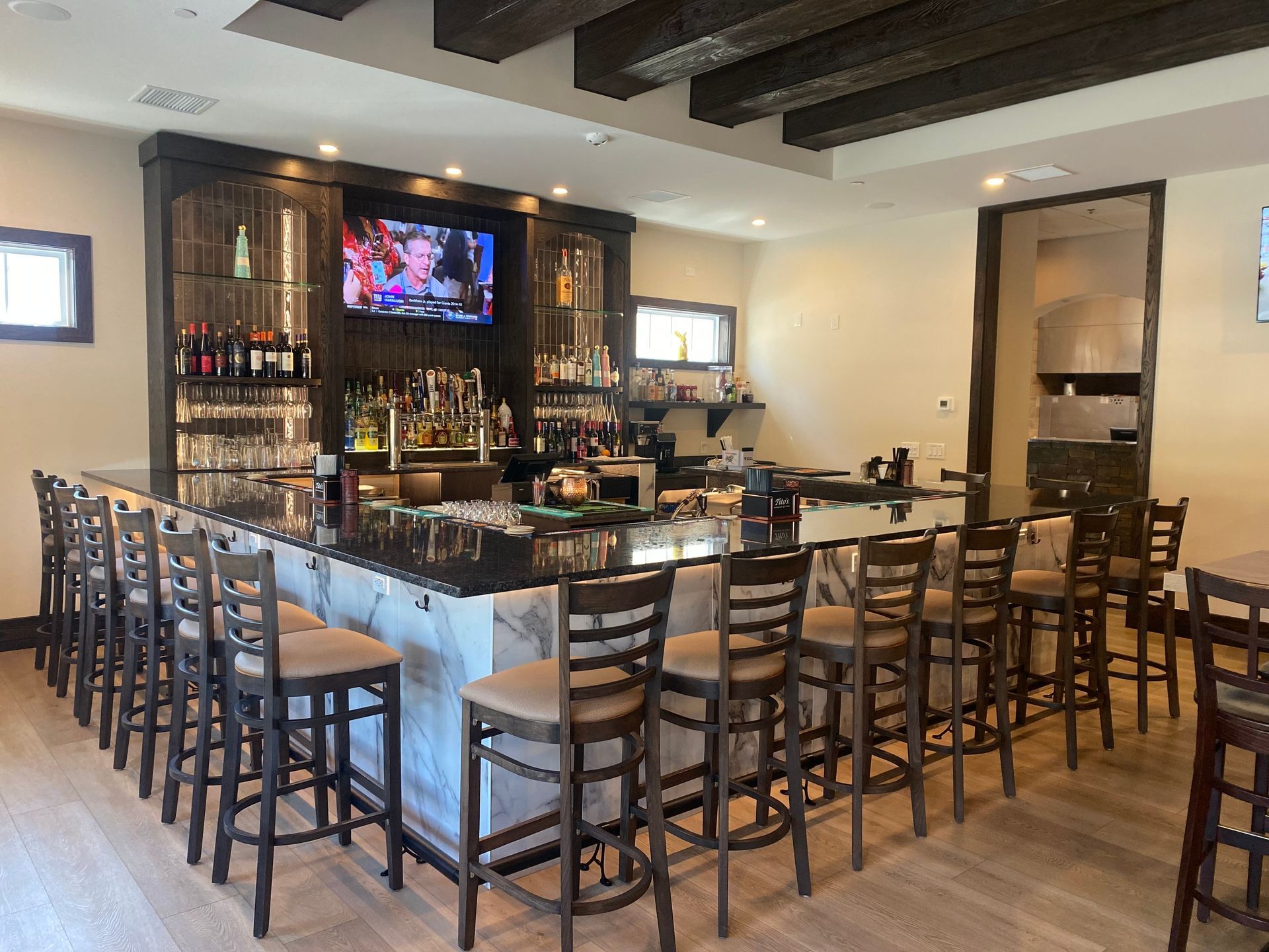 A modern bar with a black marble counter, dark wood cabinetry, and a row of tall, upholstered wooden bar stools.