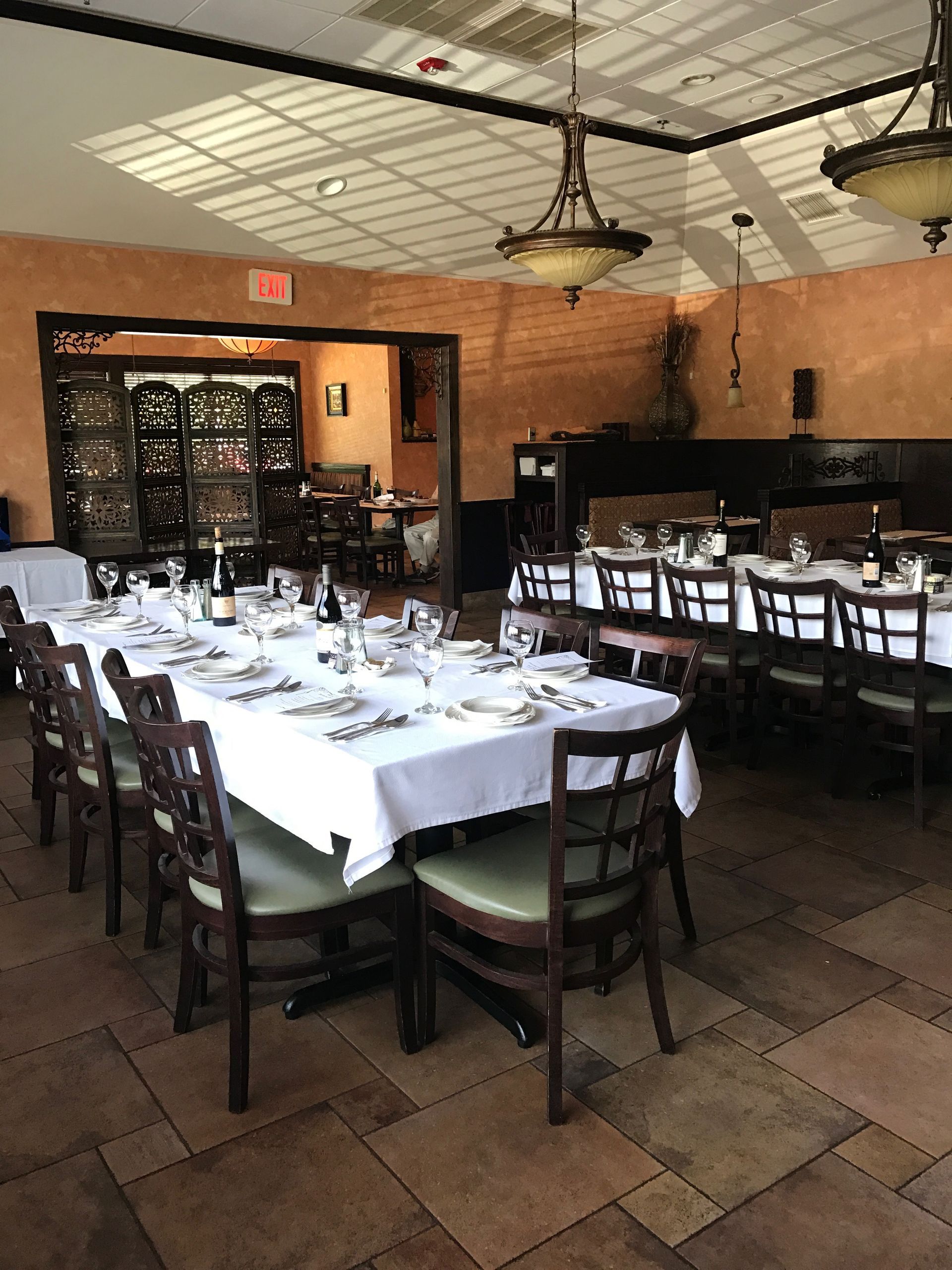 Dining room with long tables set for a meal; orange walls, tile floor, and dark wood chairs.