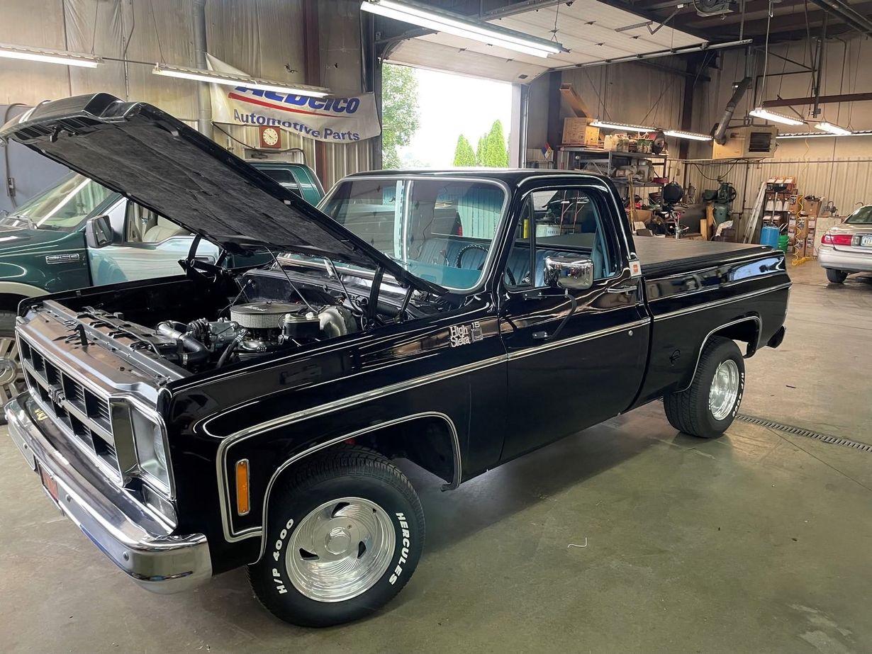 Black classic pickup truck with hood open in a garage, shown from the front-left side.