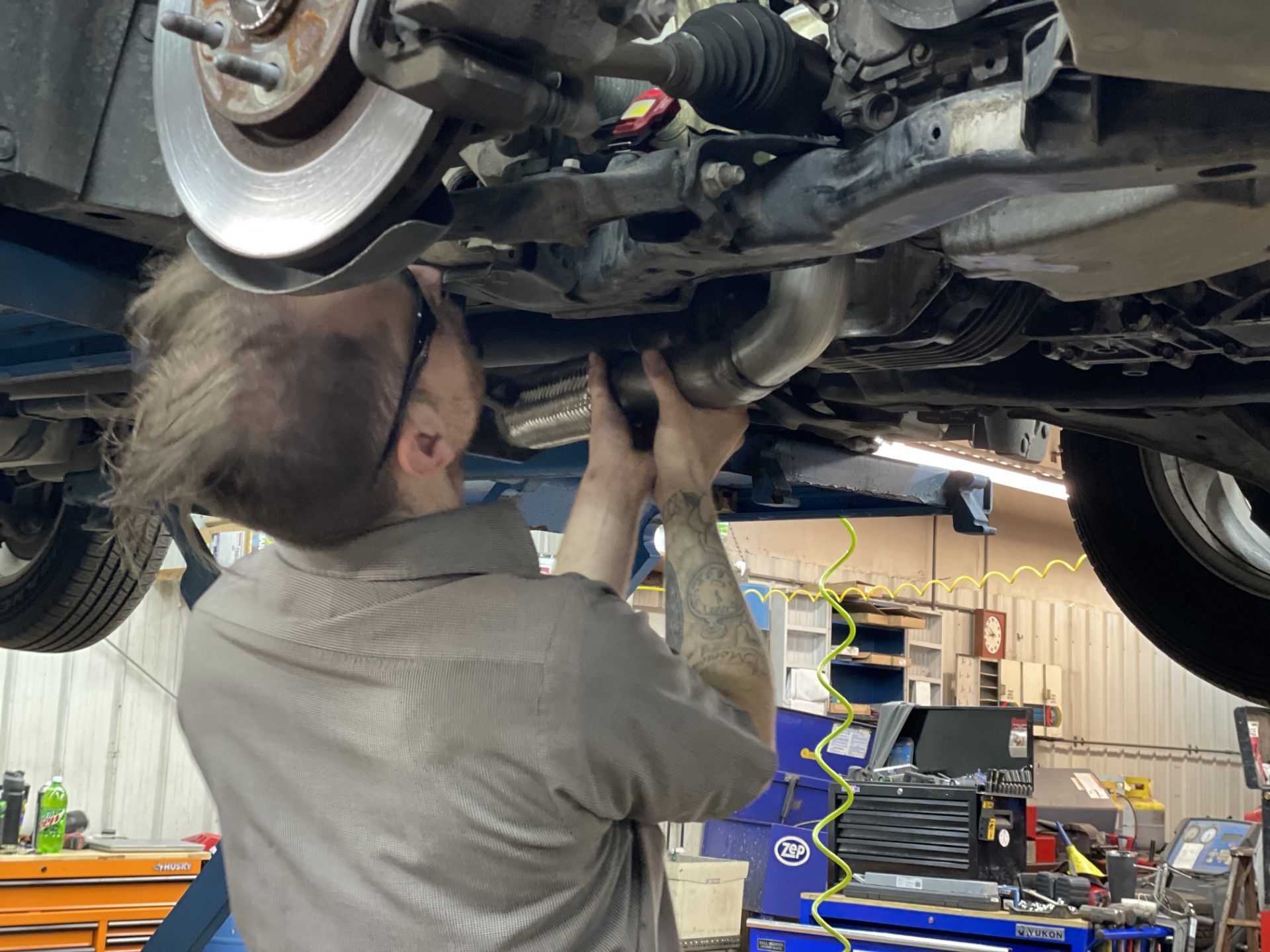 Mechanic working under a lifted car in a garage, inspecting the exhaust system.