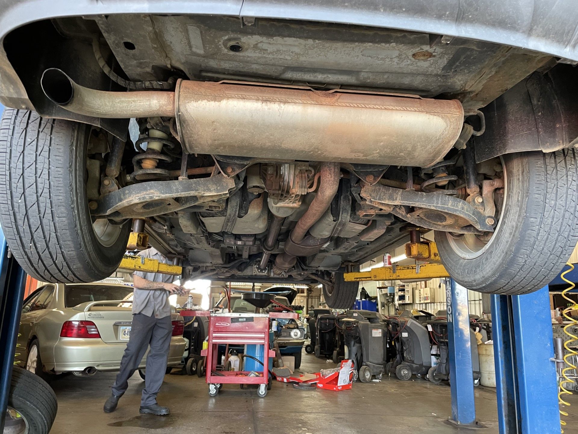 Car on a lift in an auto repair shop, underside exposed with mechanics working nearby.