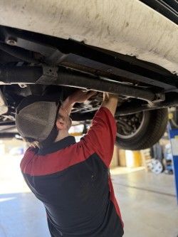 Mechanic working under a lifted car in a garage, inspecting the exhaust system.