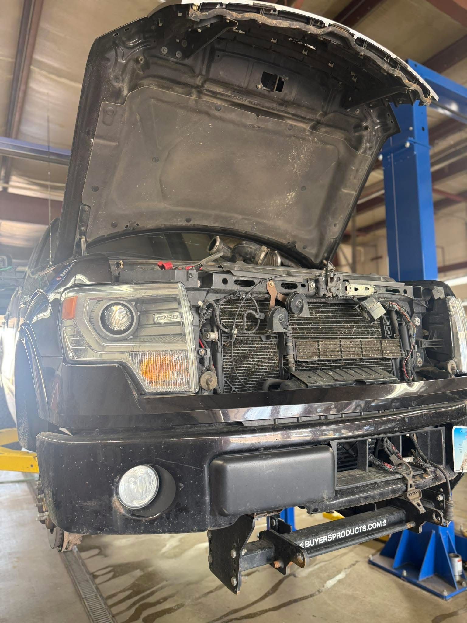 Damaged truck front end in a repair shop, hood open on a lift