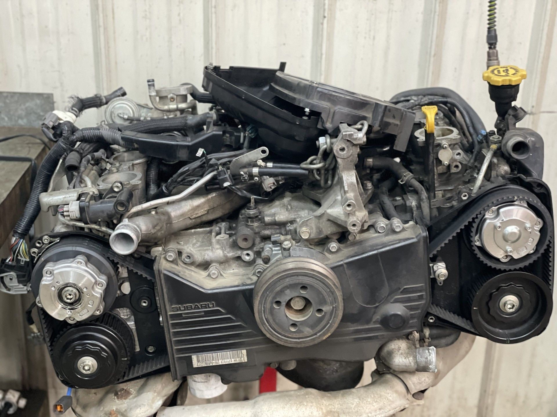 Car engine assembly with belts, pulleys, and hoses on a workshop floor