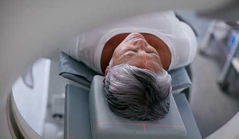 person positioned for a medical scan, head on a padded rest, inside a scanning machine