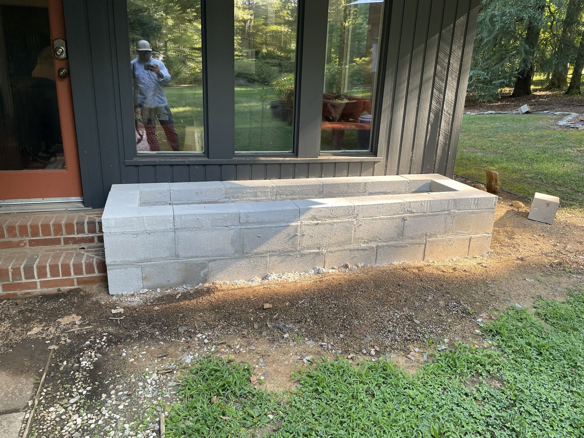 Gray cinder block planter next to a building with dark trim. A person is visible in the window.