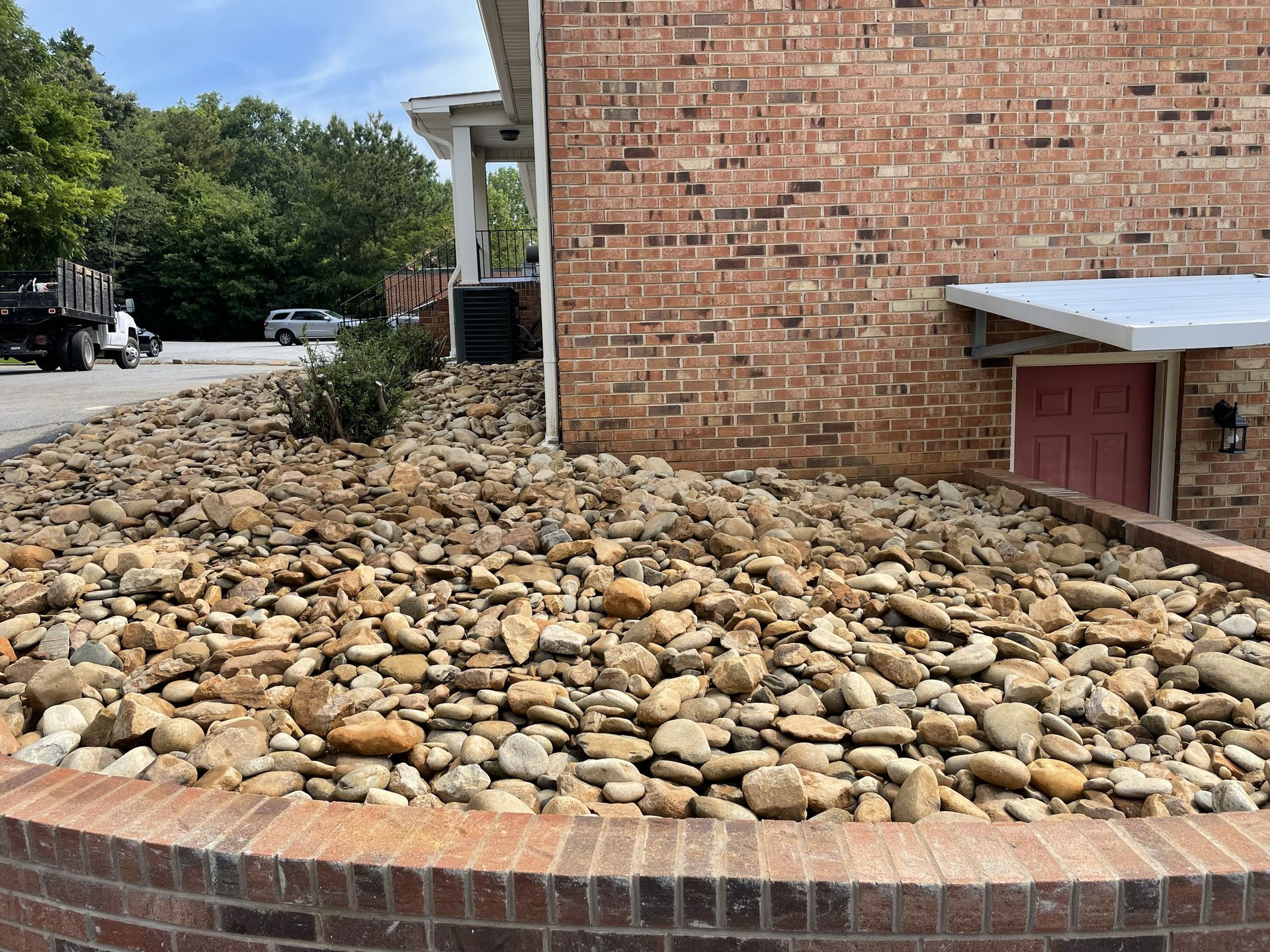 A bed of brown rocks sits against a red brick building with a brick border.
