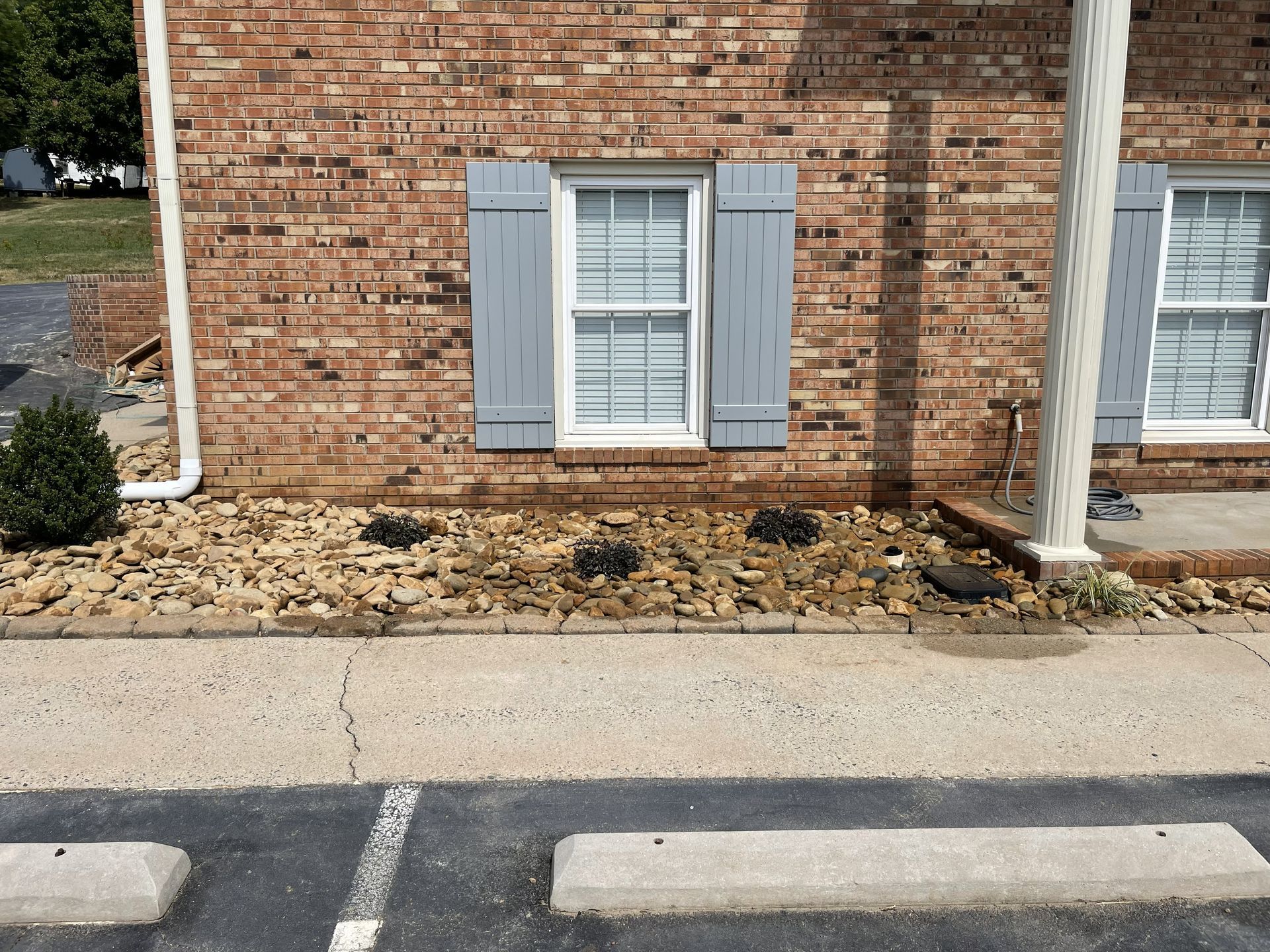 Brick building with gray shutters and a gravel flower bed next to a parking lot.