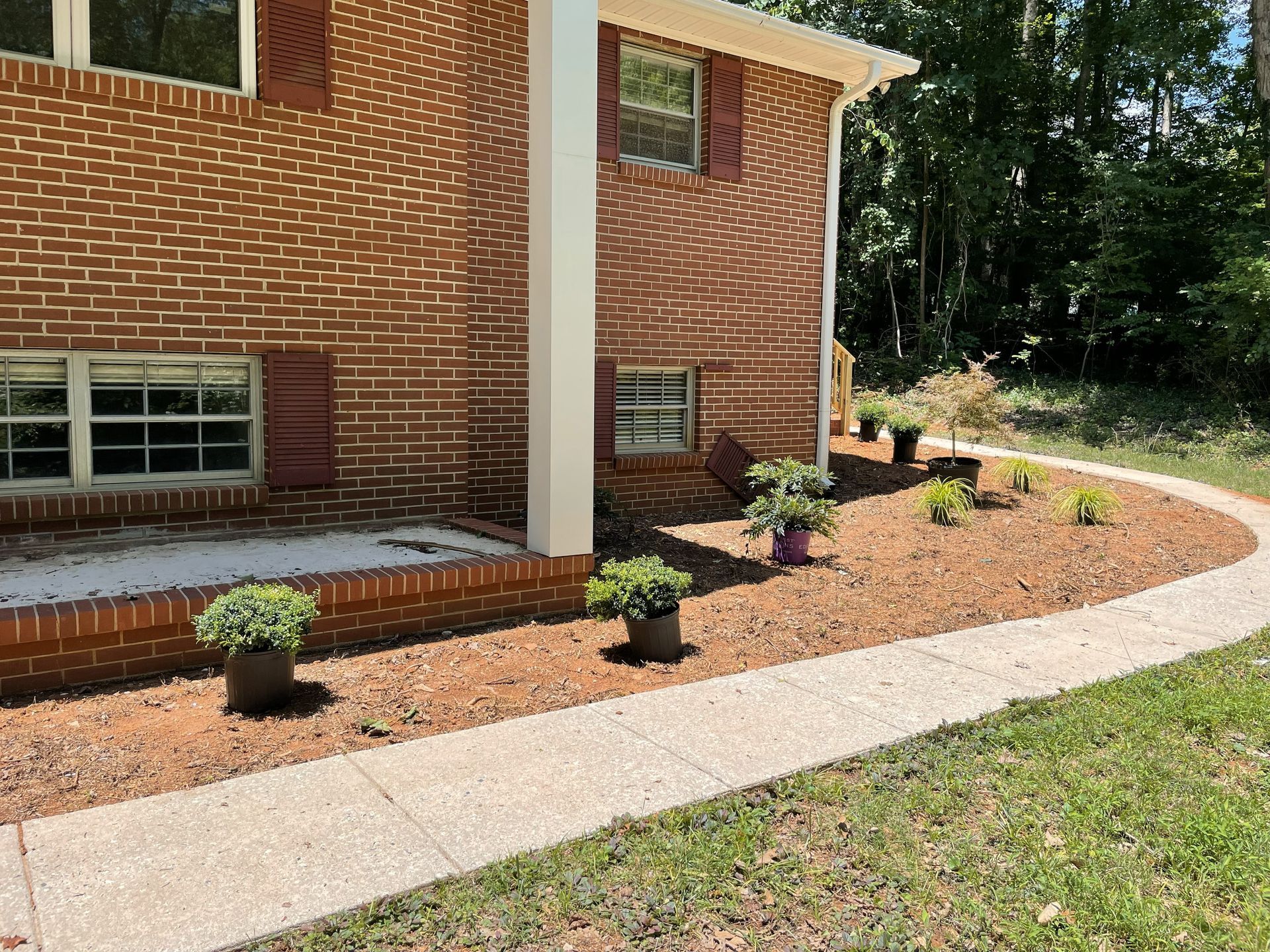 Brick house with landscaping border, concrete sidewalk, potted plants.