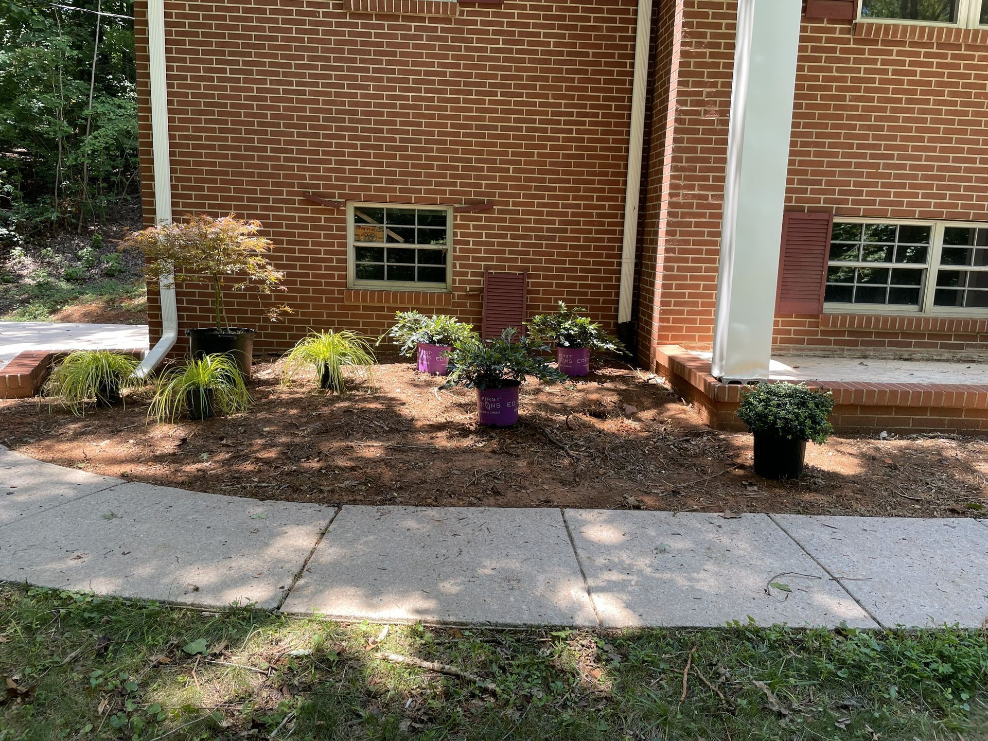 Brick building with flower beds, walkway, and landscaping. Purple pots with flowers.